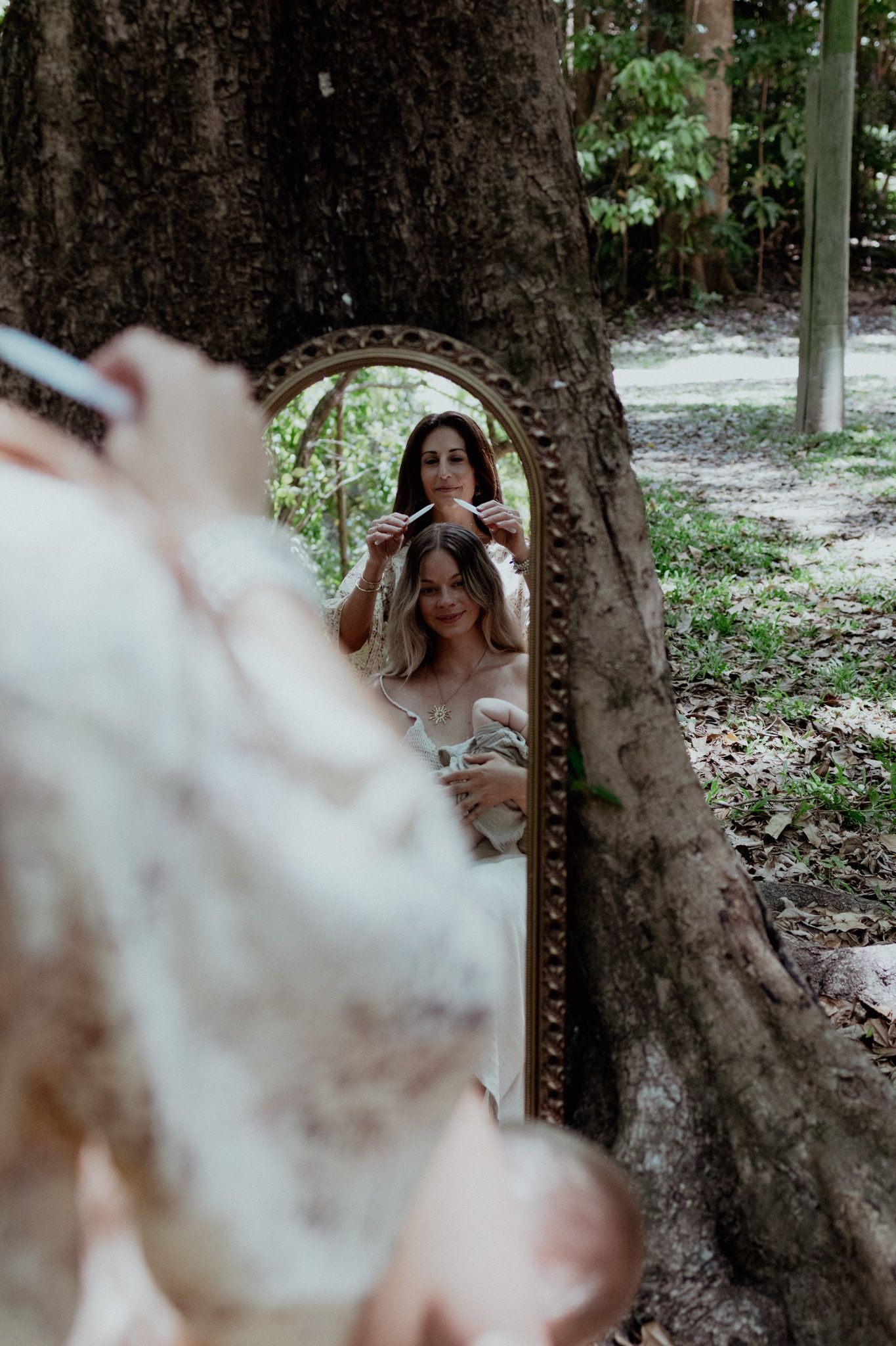 A vintage mirror propped against a tree reflects a peaceful outdoor scene.