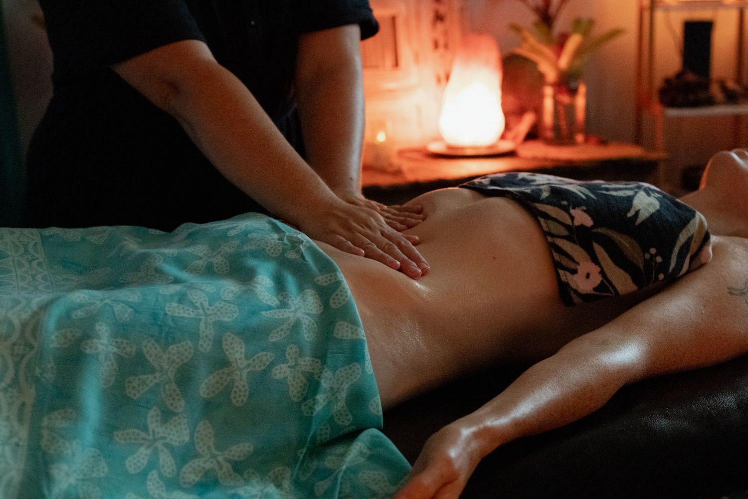 Massage therapist gently massaging a client's abdomen during a relaxing spa treatment in a candlelit room with warm ambient lighting.
