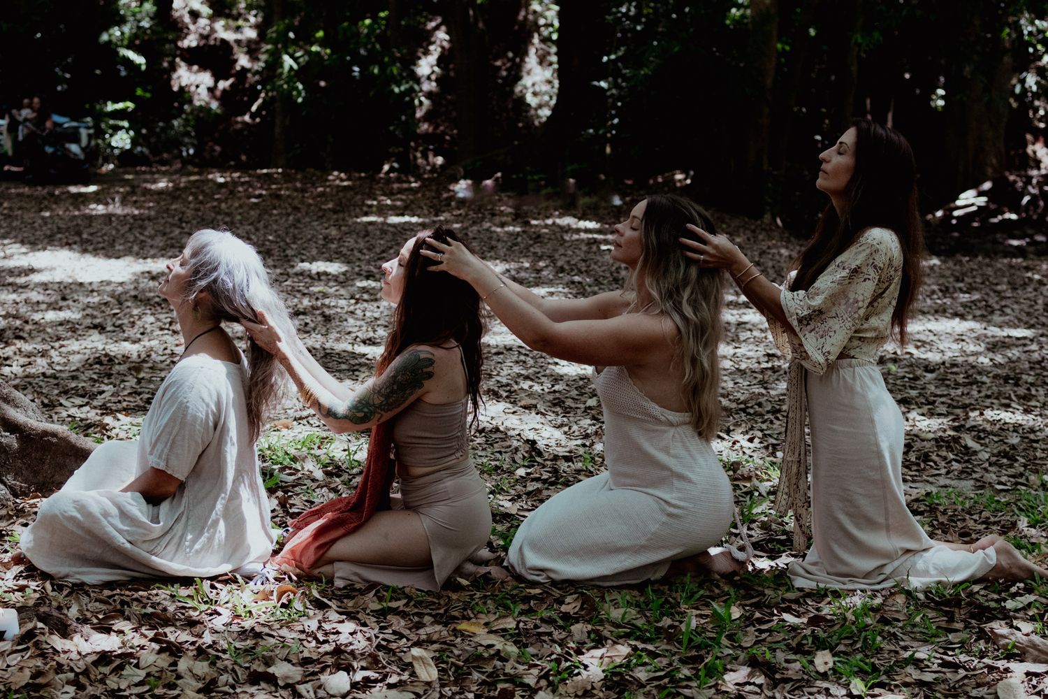 Dreamy sequence of people in white dresses sitting together on forest ground.