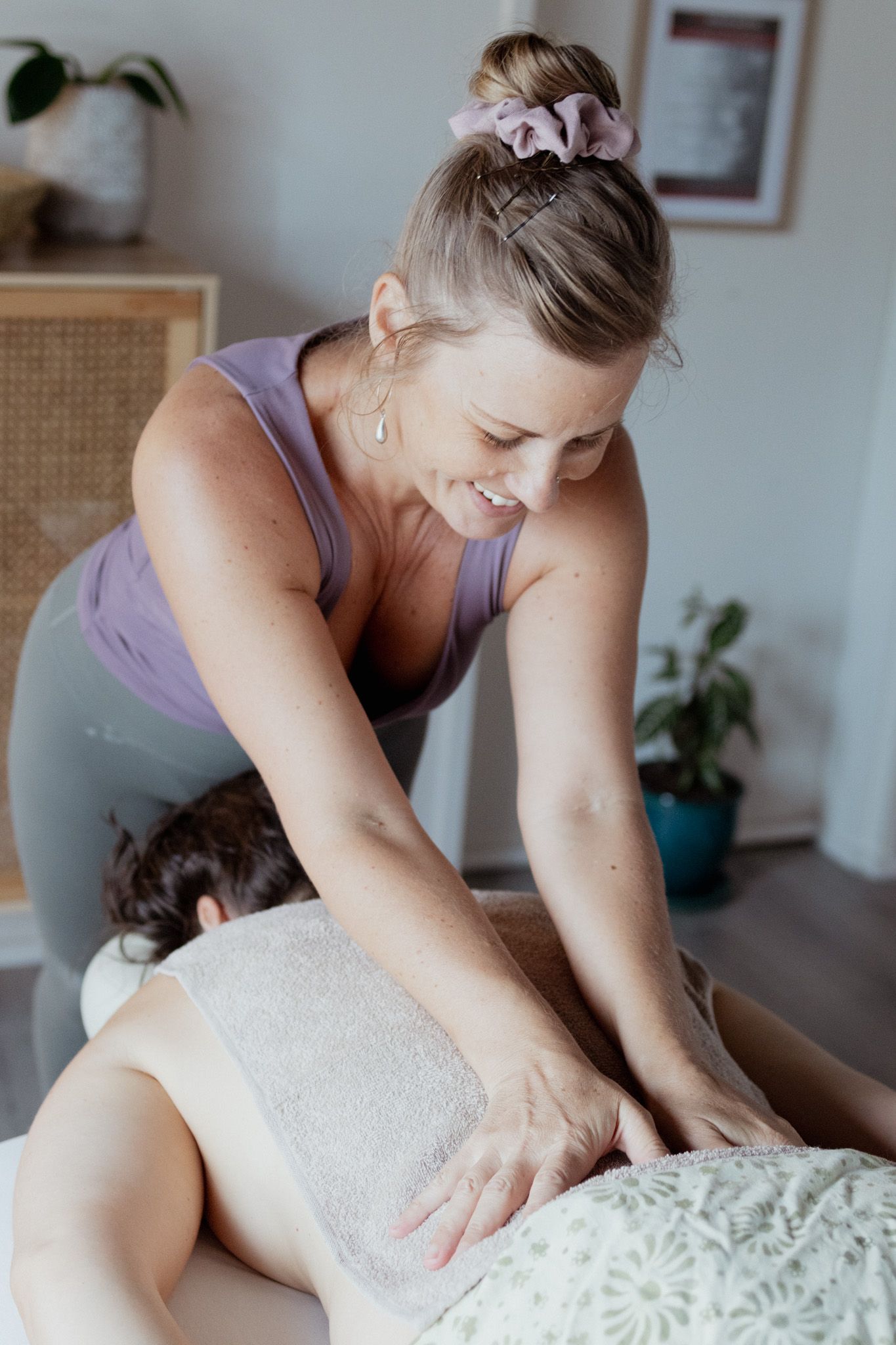 Professional masseuse wearing purple top applies pressure during therapeutic massage session.