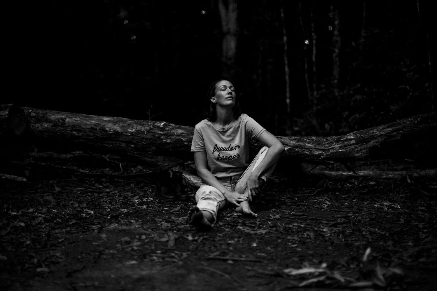 Moody black and white forest scene with a person resting on natural elements.
