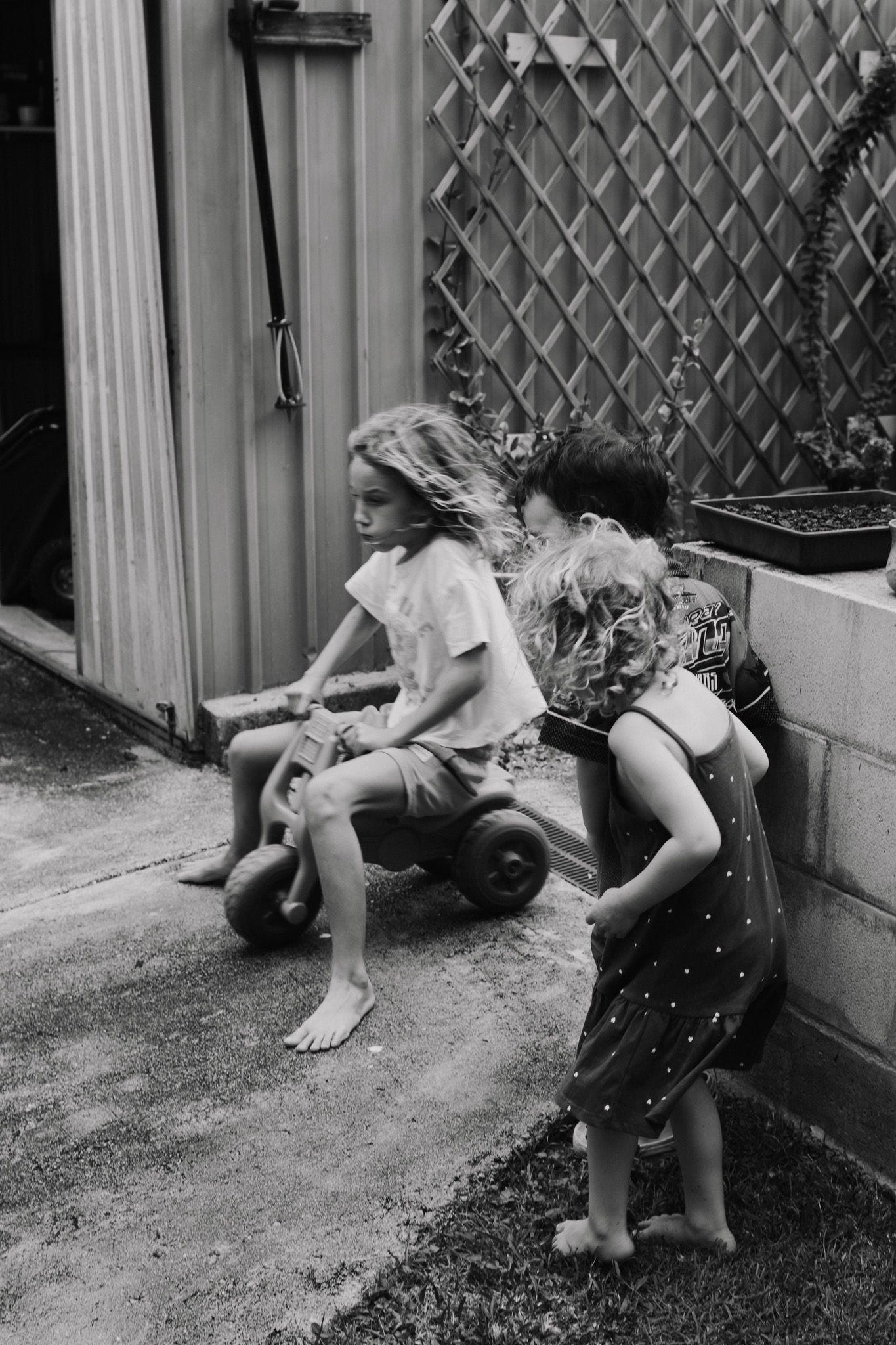 Black and white image of children playing on a toy vehicle outdoors.