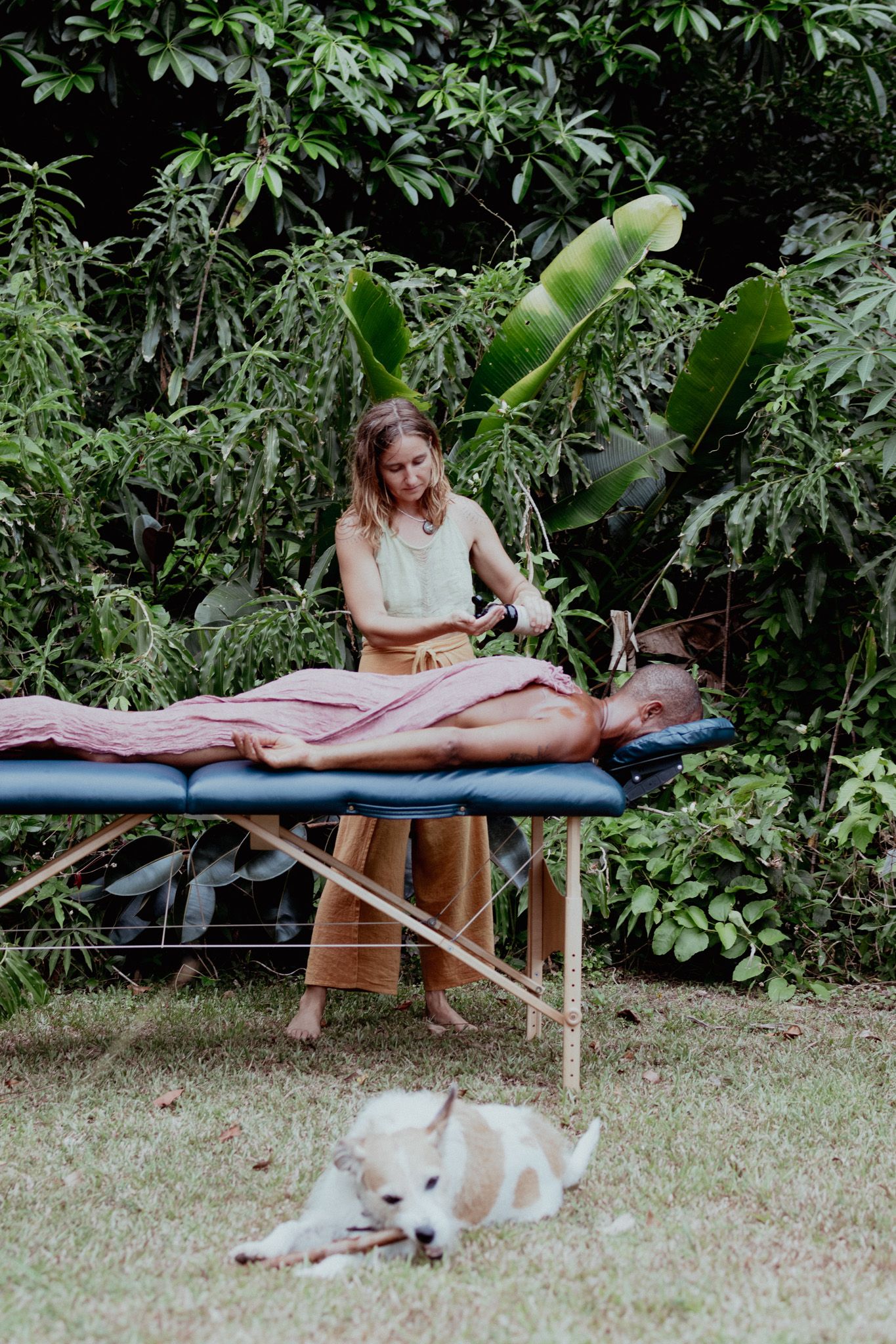 A peaceful outdoor massage scene with a white dog lounging in the background.