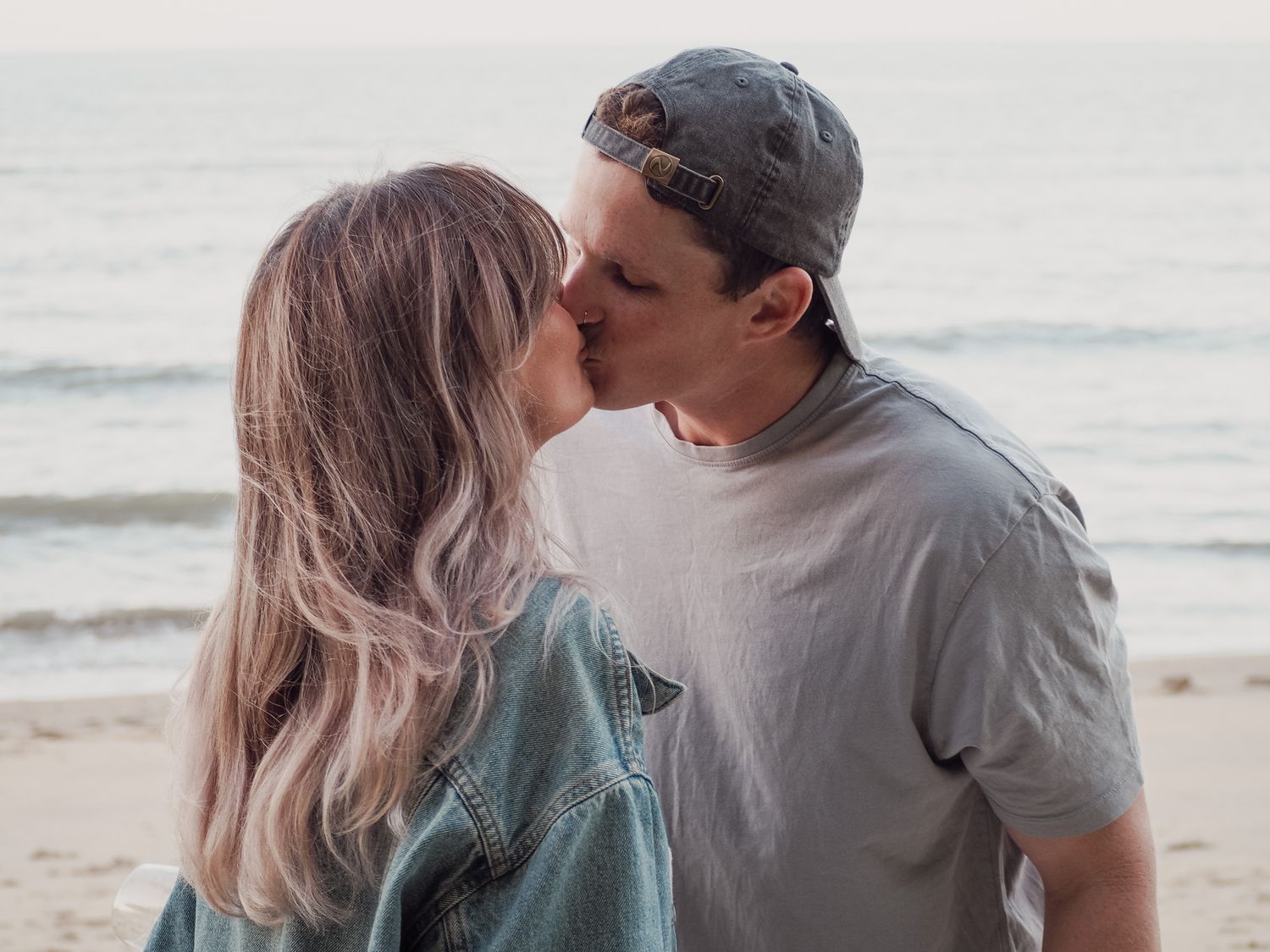 Romantic couple sharing intimate moment on beach with ocean waves in background.