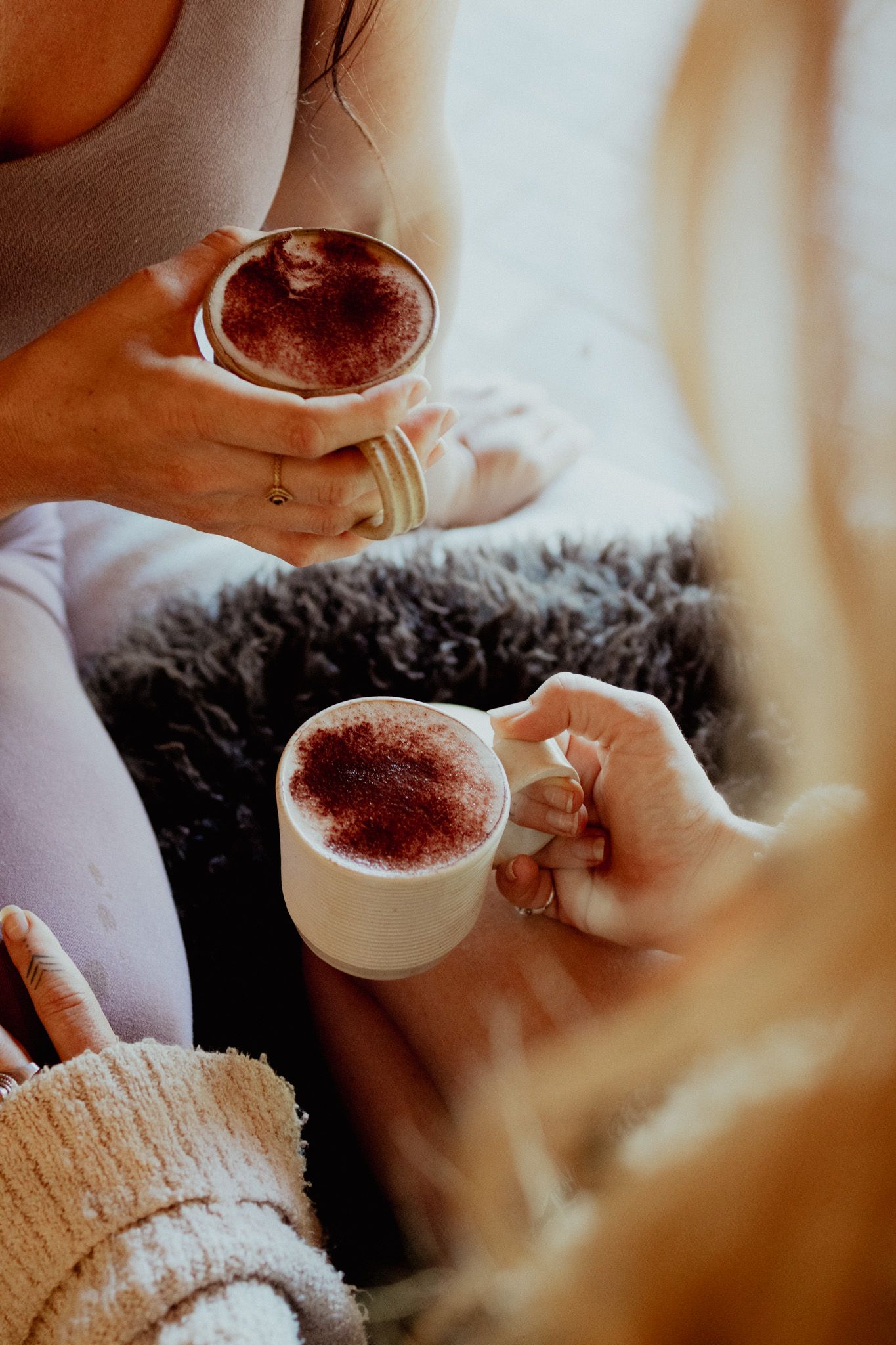 Hands holding cups of coffee with cocoa powder being sprinkled on top.