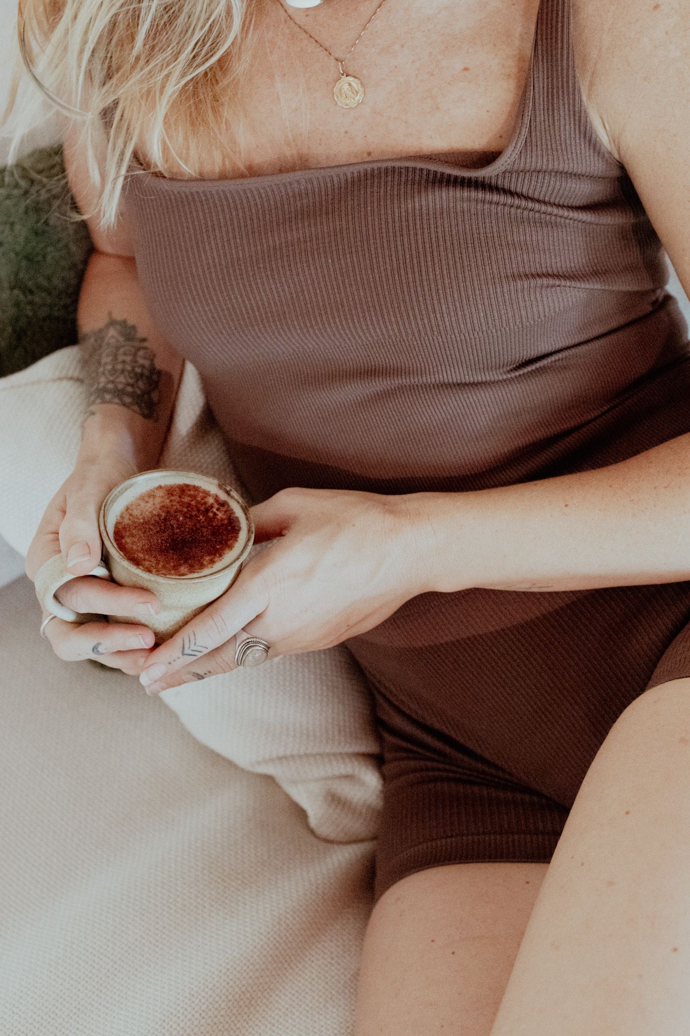 Person in beige top holding a small ceramic cup while relaxing.