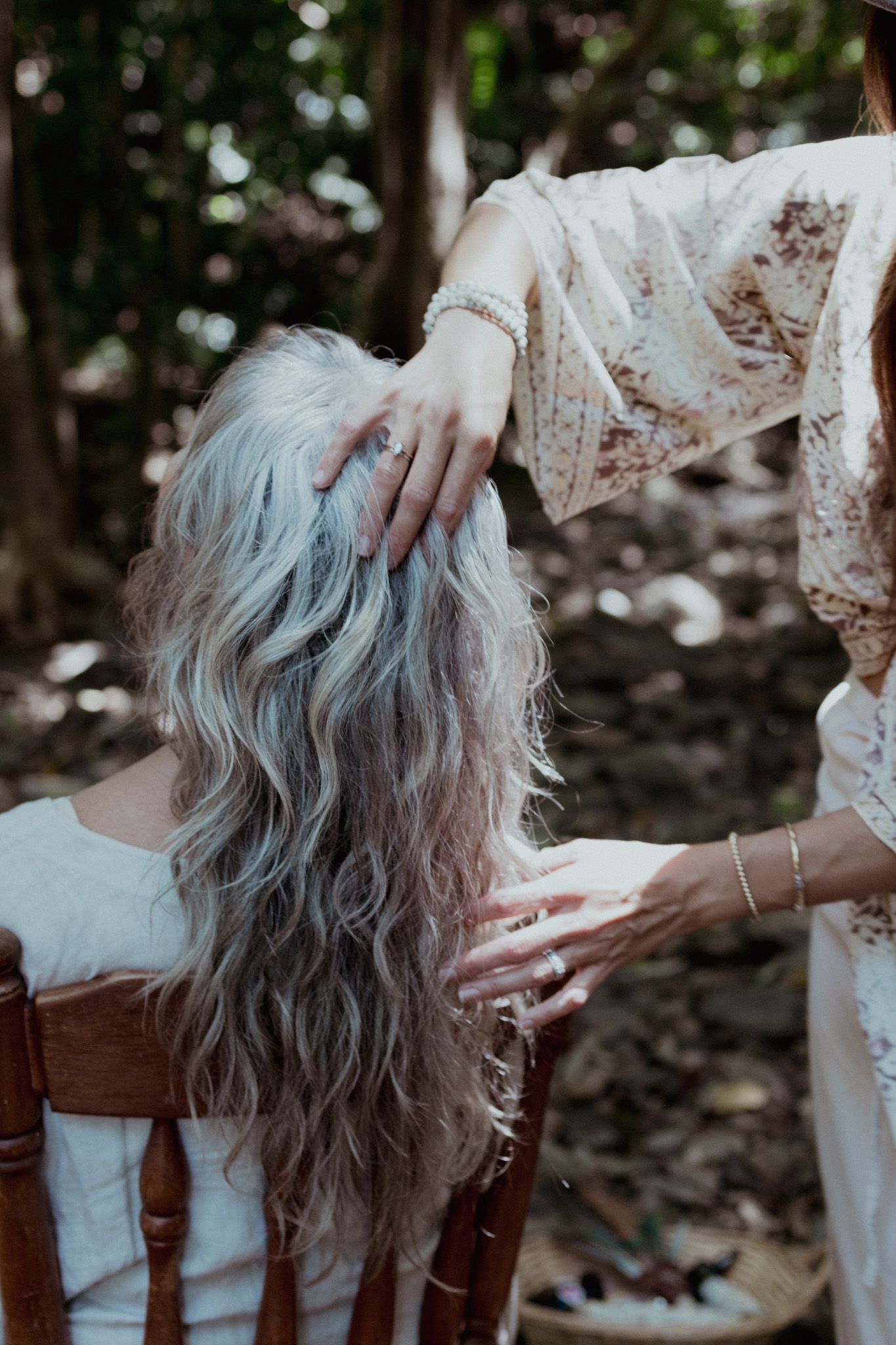 Silver-haired figure rests peacefully while another person in lace gently touches their hair.