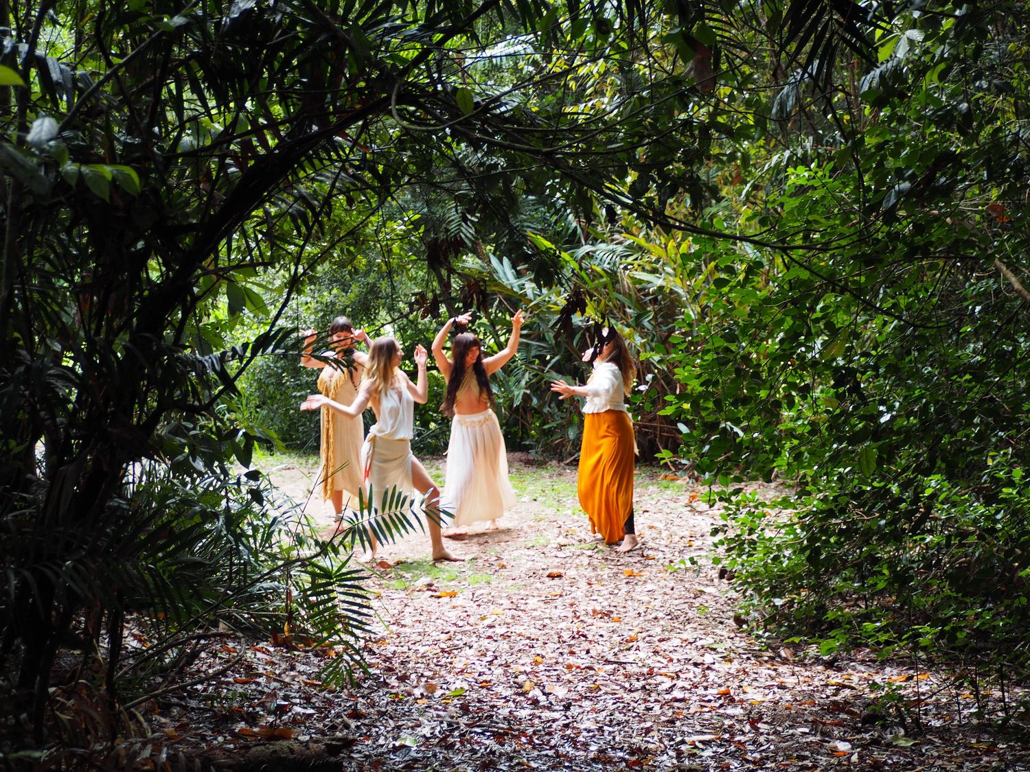 People in white and orange dresses walk along a garden path surrounded by tropical foliage.