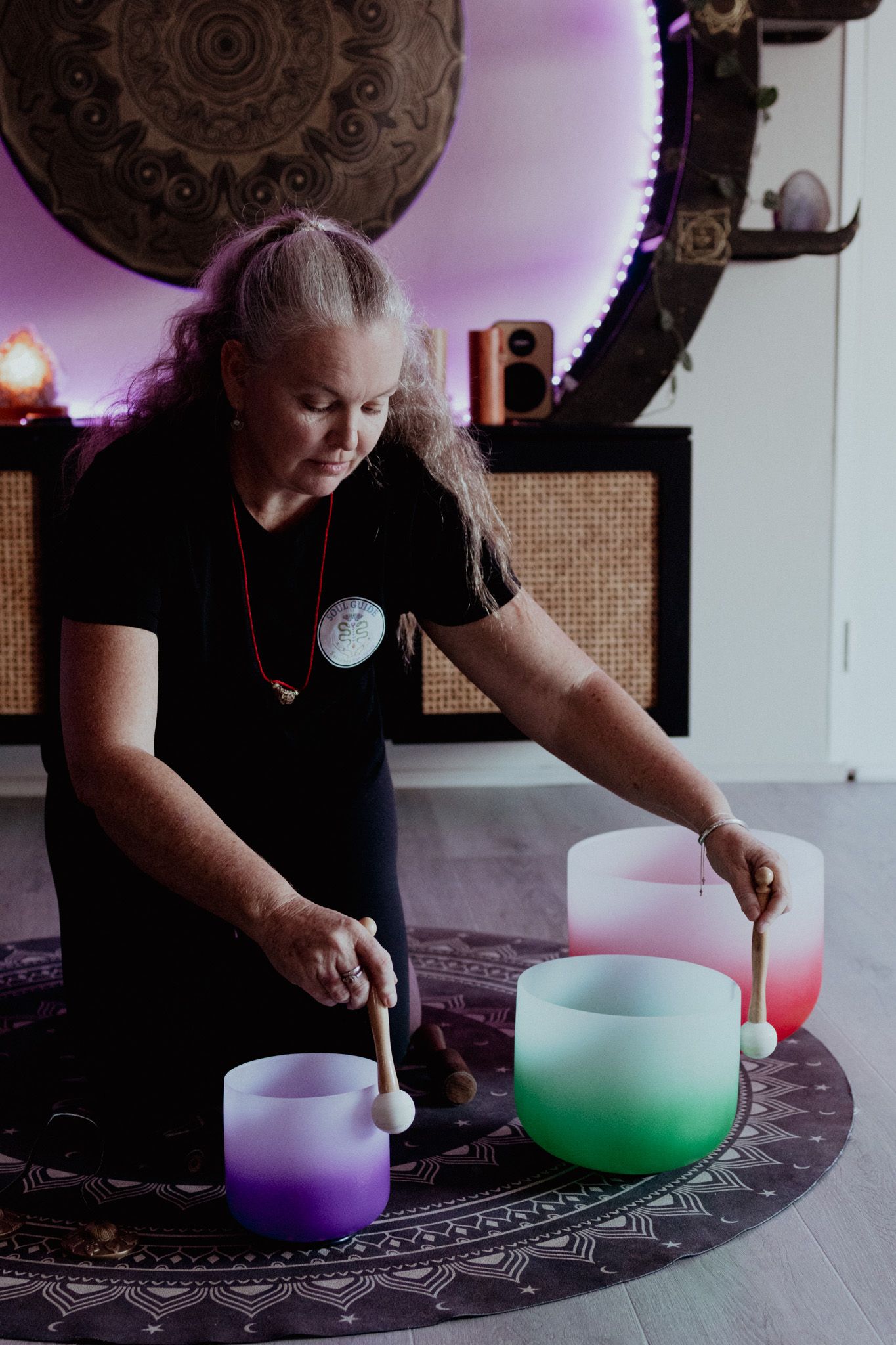 Crystal singing bowls being played on a patterned mat with colorful lighting effects.