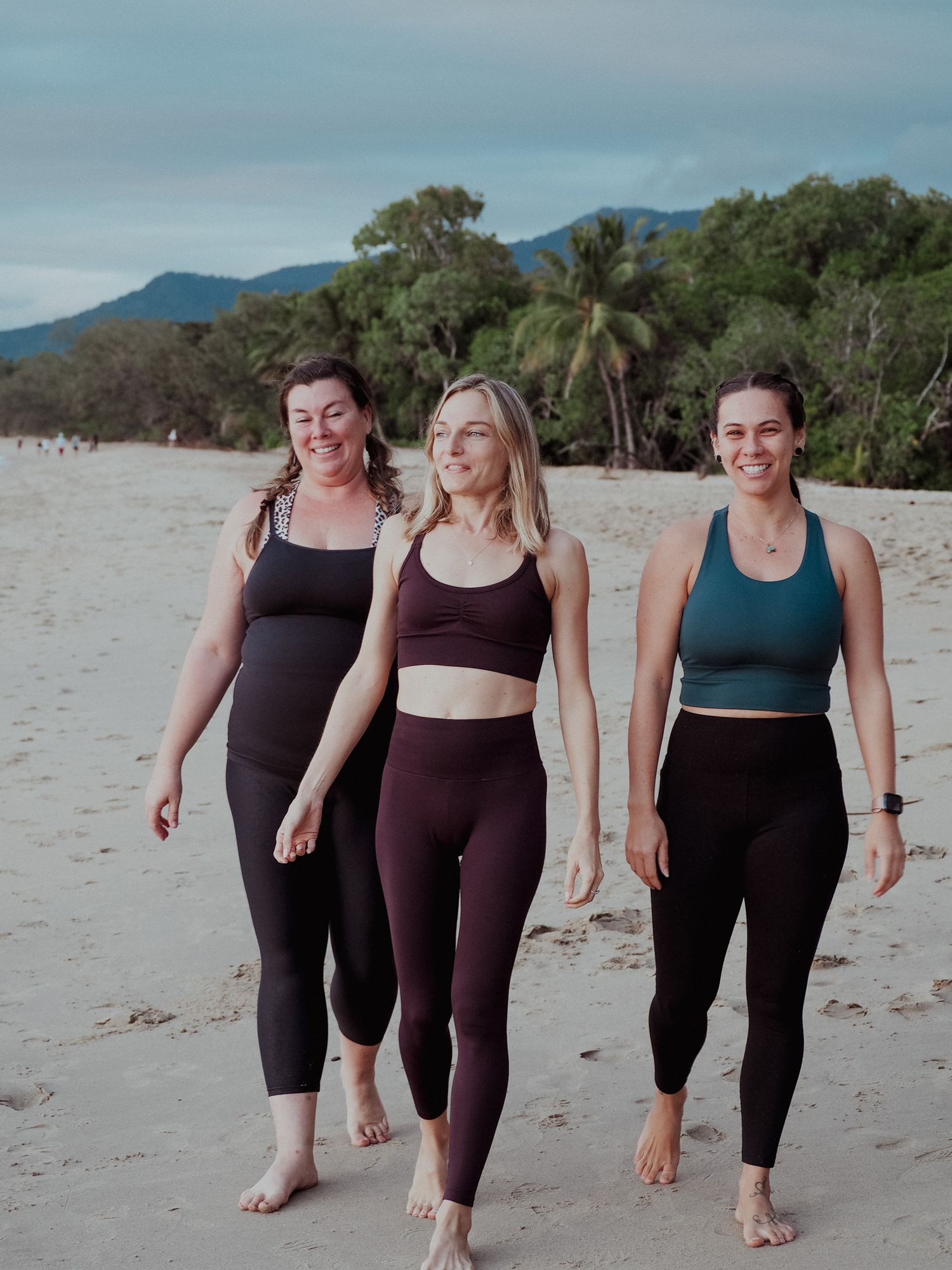 People in athletic wear walk together on a beach with mountains in the background.