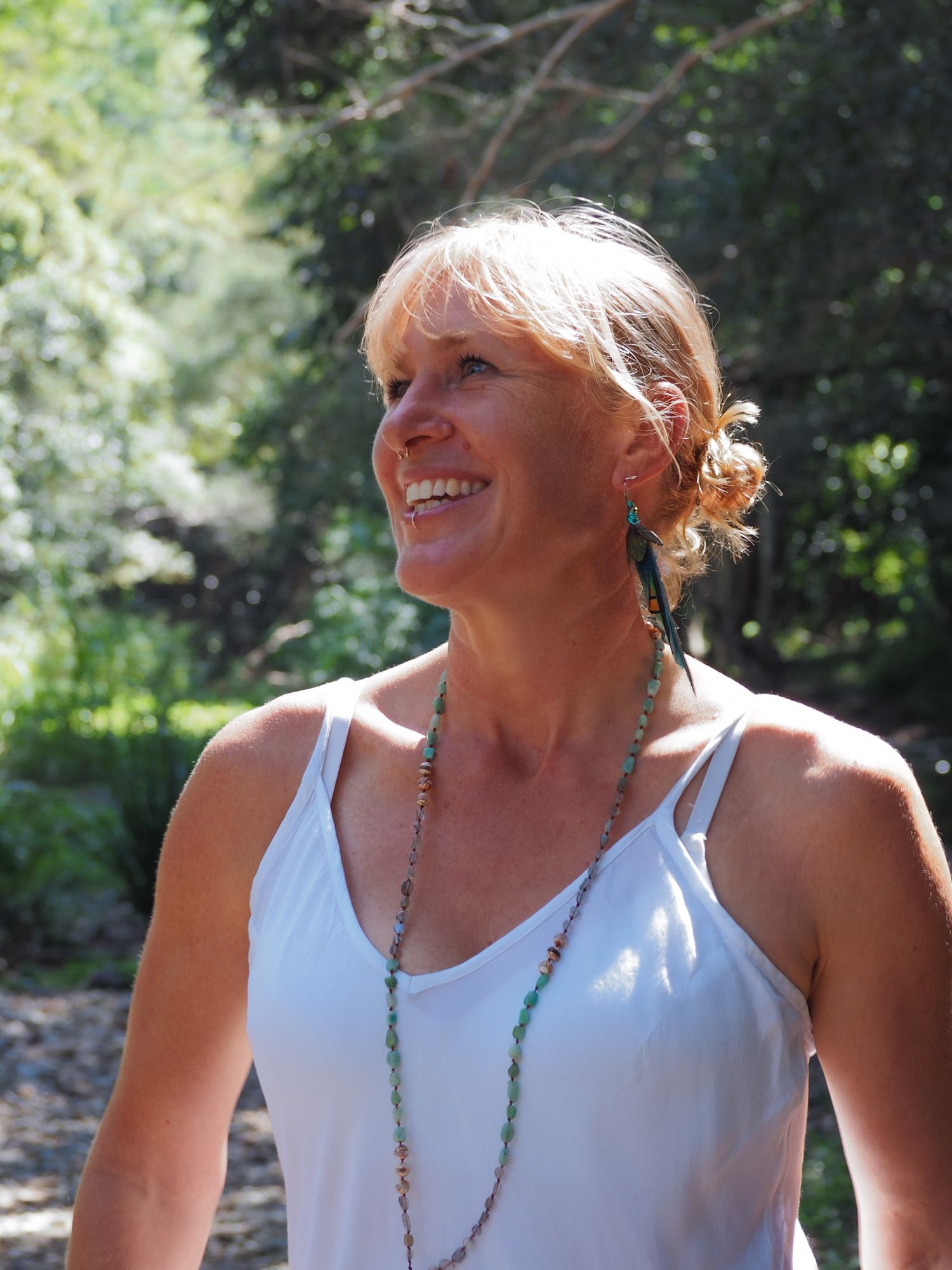 Person in white tank top with turquoise necklace enjoying sunshine outdoors.