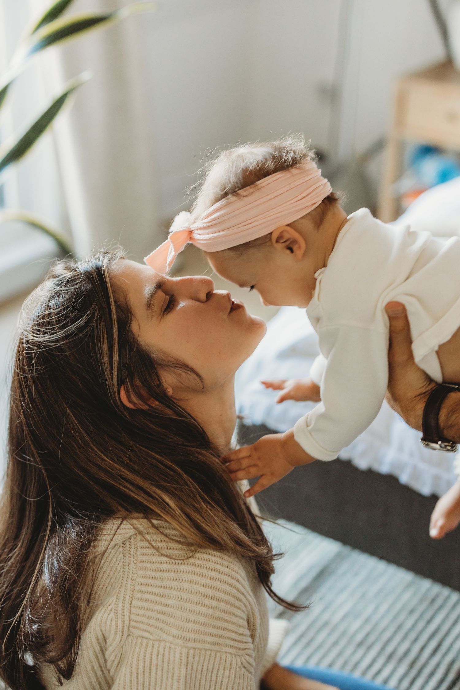 Loving mother lifting her baby girl close for a gentle nose kiss in a bright, warmly lit room.