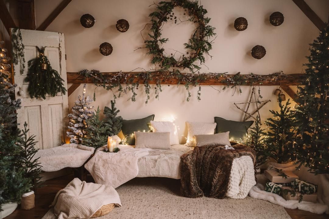 Cozy Christmas bedroom with decorated trees, wreath, garlands, candles, and festive holiday decor in a warm rustic setting.