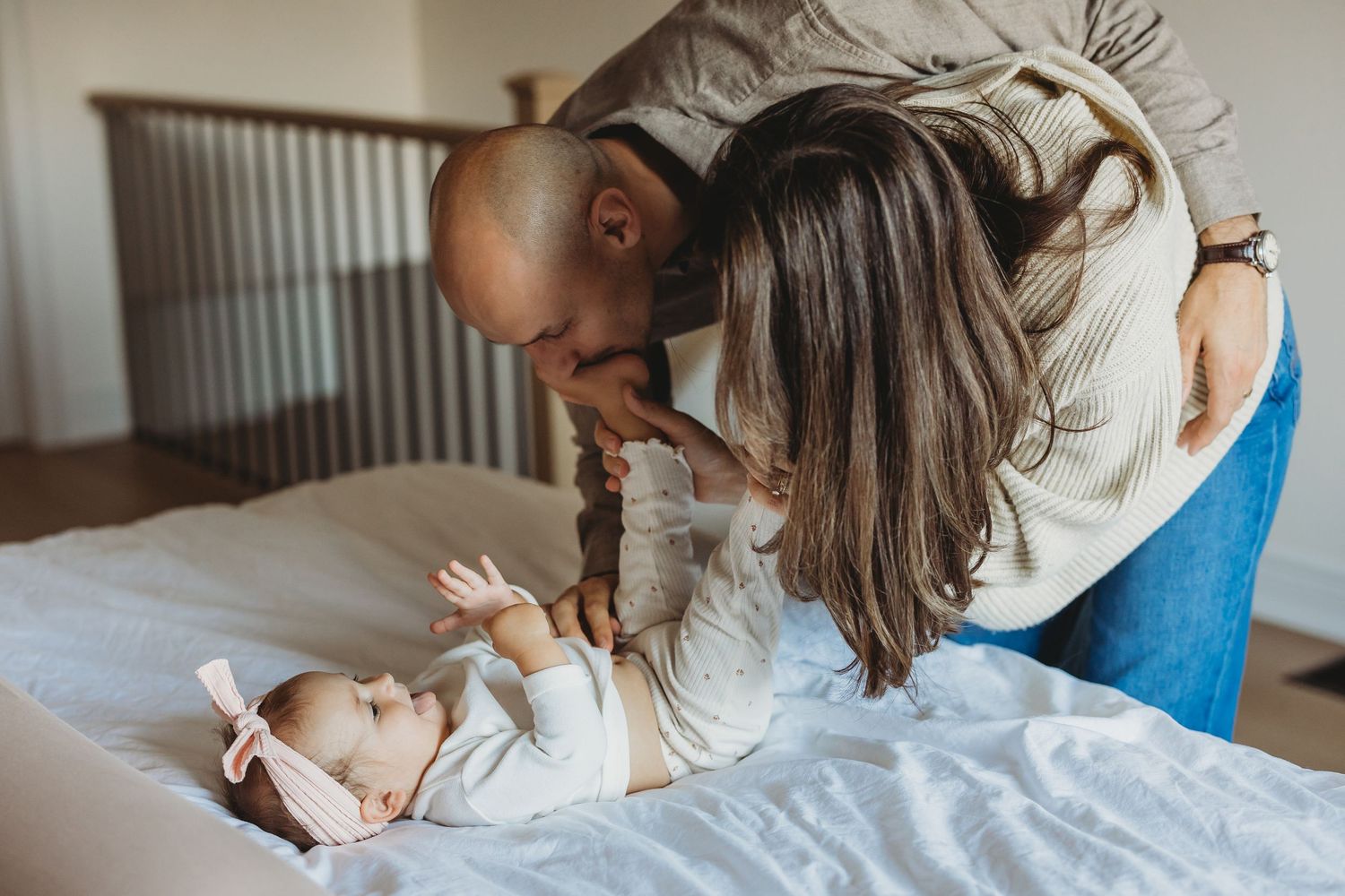 Parents lovingly kiss their newborn baby lying on a bed, capturing a tender family bonding moment. Family moments.