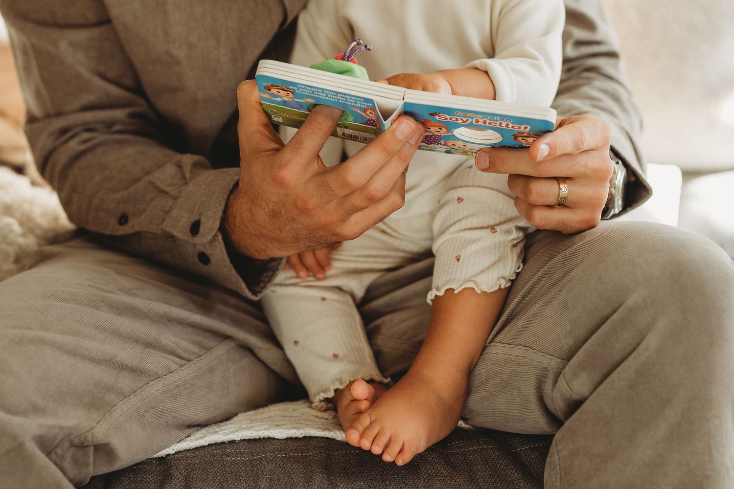 Adult reading a colorful board book to a baby sitting on their lap, promoting early childhood literacy. Father and daughter.