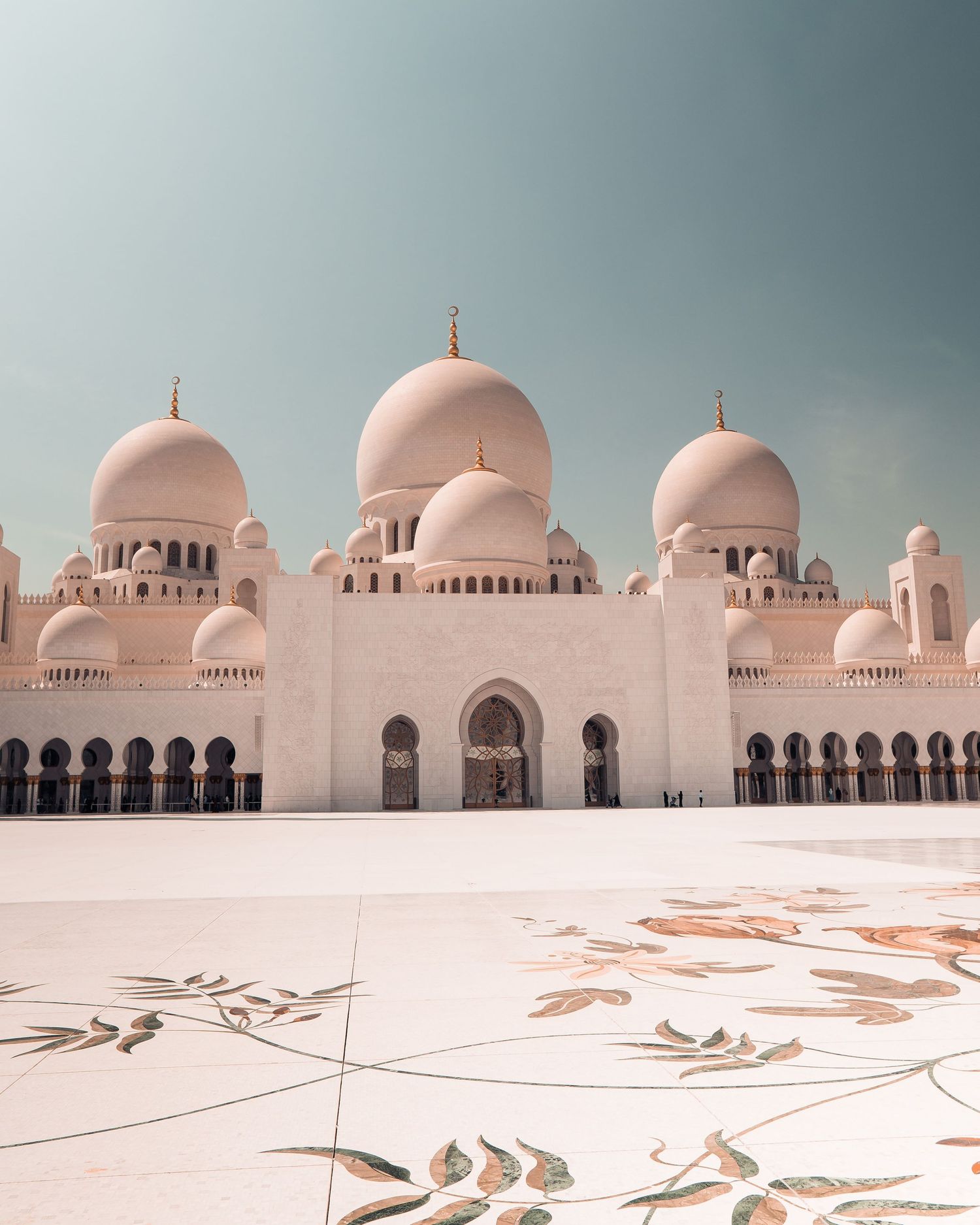 White domes and arches of Sheikh Zayed Grand Mosque in Abu Dhabi against a moody sky with geometric floor patterns.