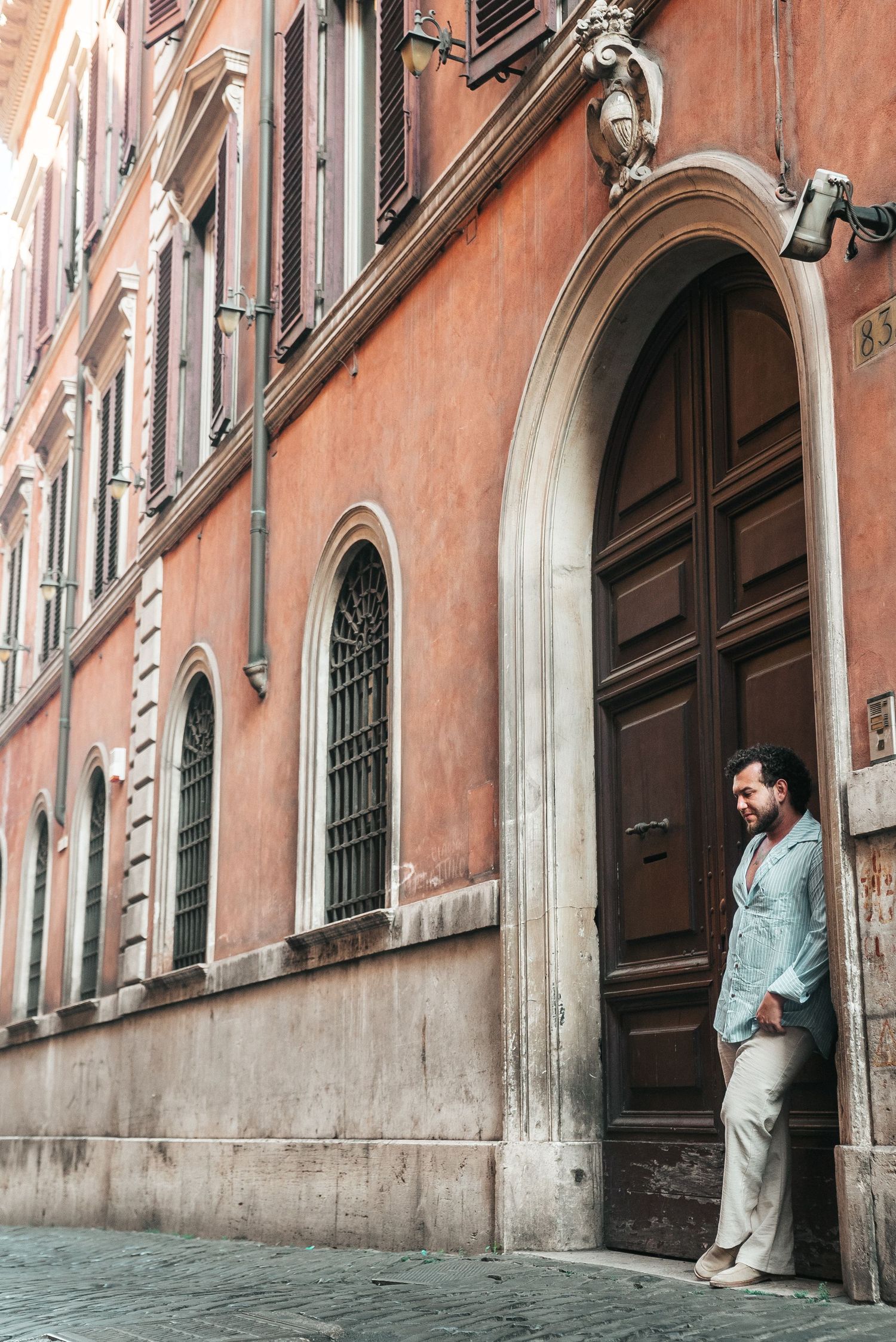 Tourist standing in doorway of traditional terracotta-colored Italian building with arched entrance.