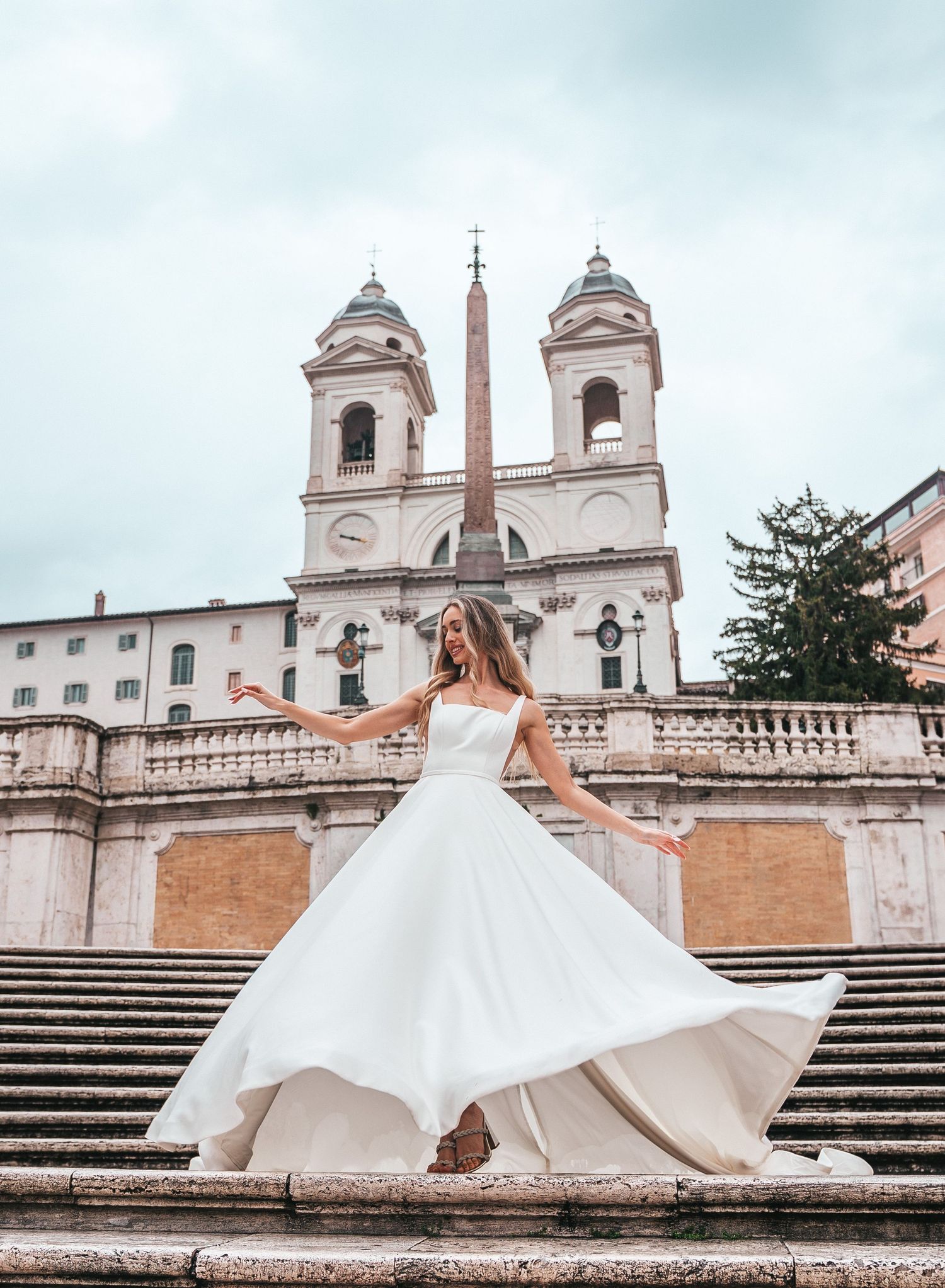 Flowing white wedding dress twirls on the Spanish Steps with church towers in background.