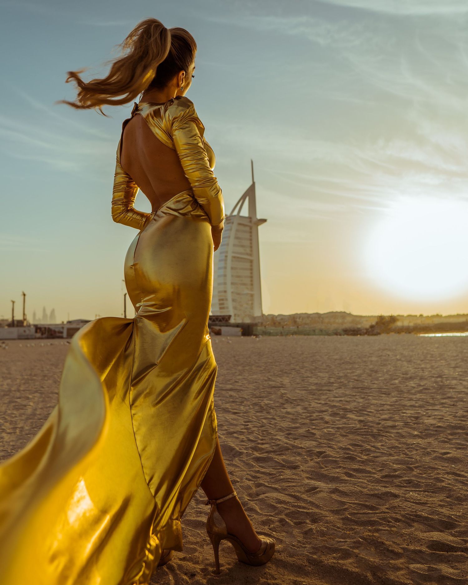 A flowing yellow dress catches the sunlight against the iconic Burj Al Arab hotel backdrop in Dubai at sunset.