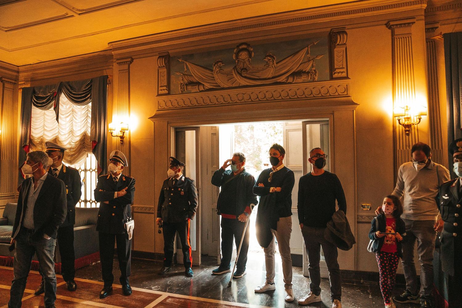 People stand in a line inside an ornate historic building with warm lighting and elegant architectural details.