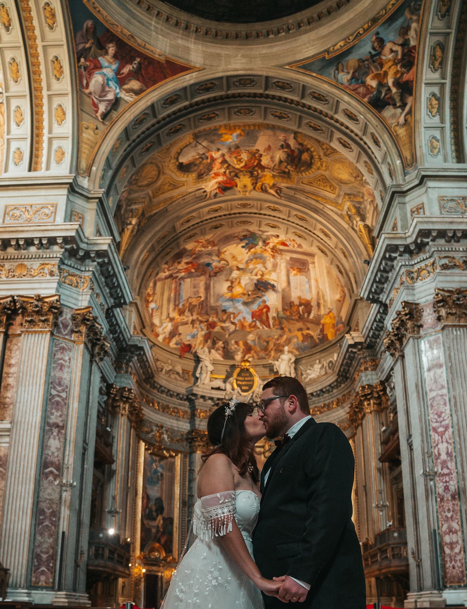 Romantic wedding photo inside an ornate cathedral with stunning baroque ceiling frescoes.