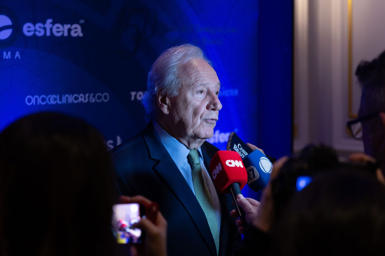 A person speaks into a microphone at a podium during a darkly lit event.