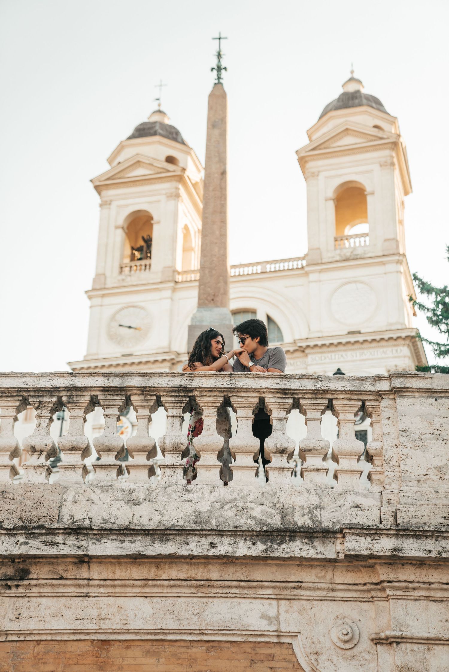 Couple posing on historic Spanish Steps with white church towers in background.