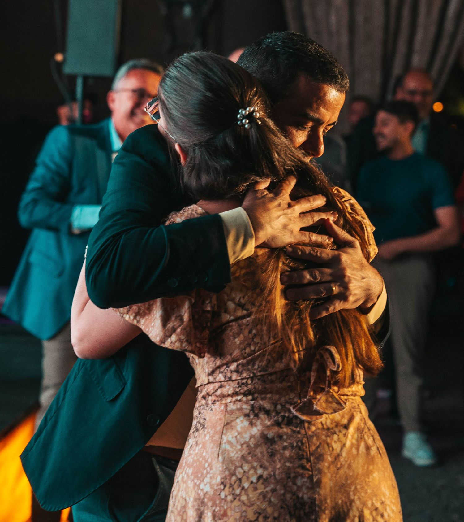 A couple dances intimately in a dimly lit venue with warm ambient lighting creating a romantic atmosphere.