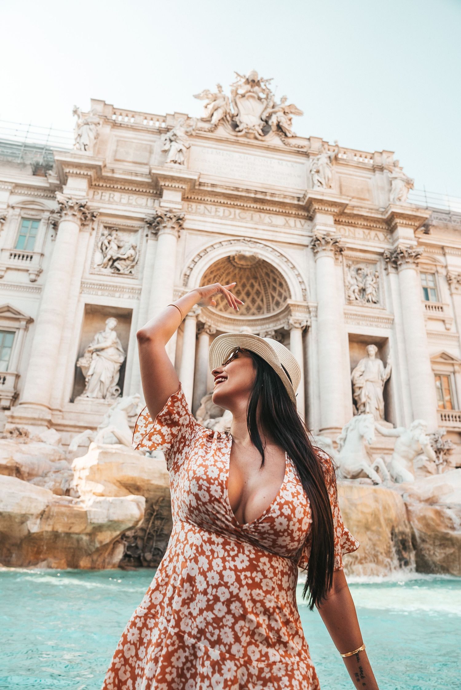 Tourist in floral dress posing joyfully at the baroque Trevi Fountain in Rome.