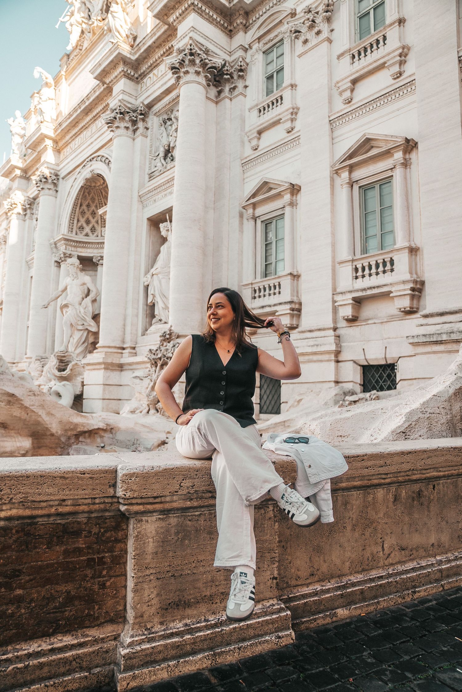 Tourist enjoying moment at Trevi Fountain in Rome wearing black and white outfit.