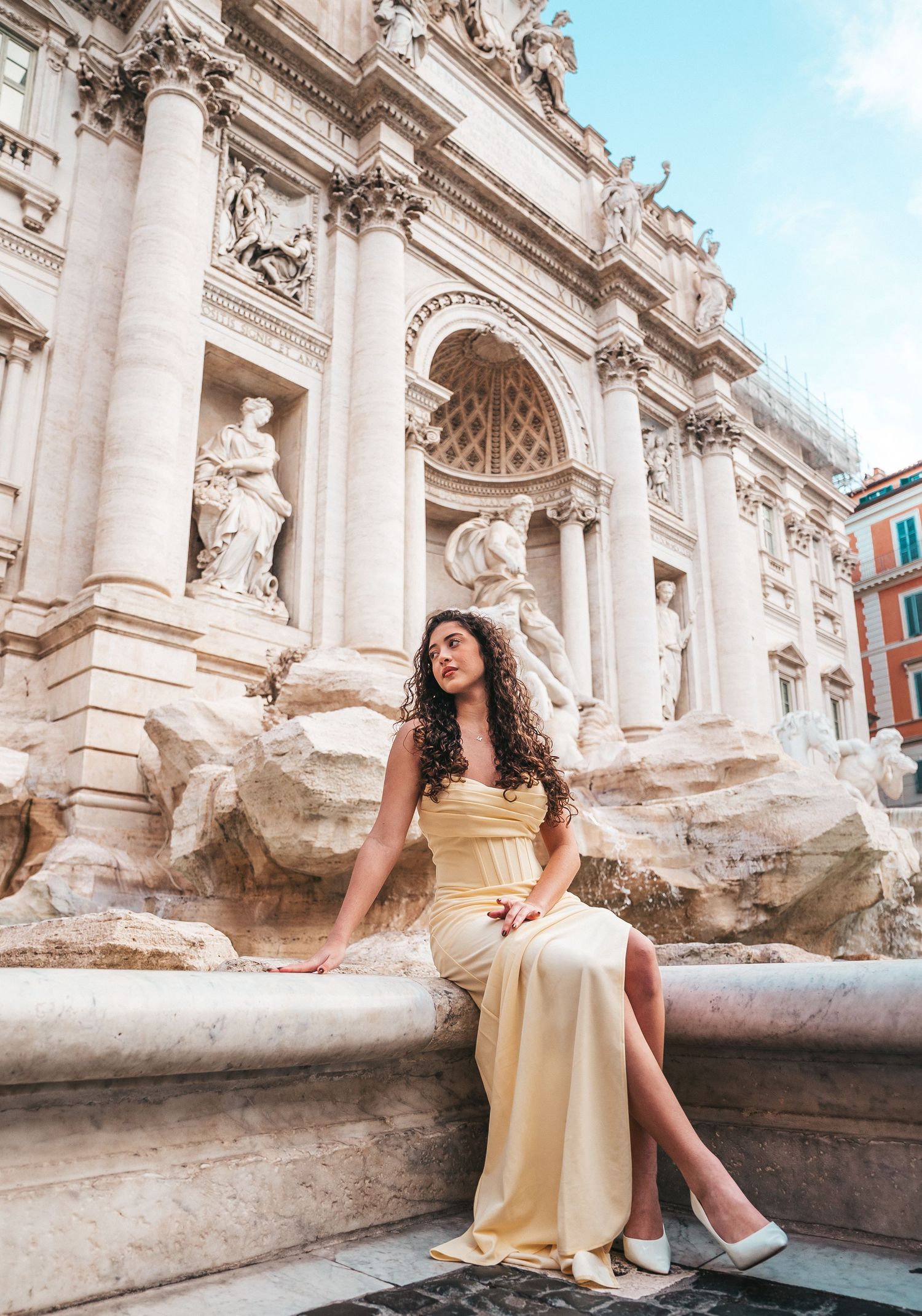 Woman in gold dress sitting at the edge of Trevi Fountain in Rome.