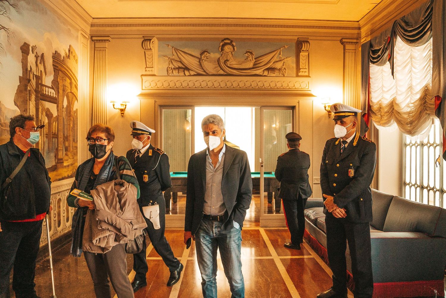 People gather in an elegant hallway with ornate decorations and warm lighting.