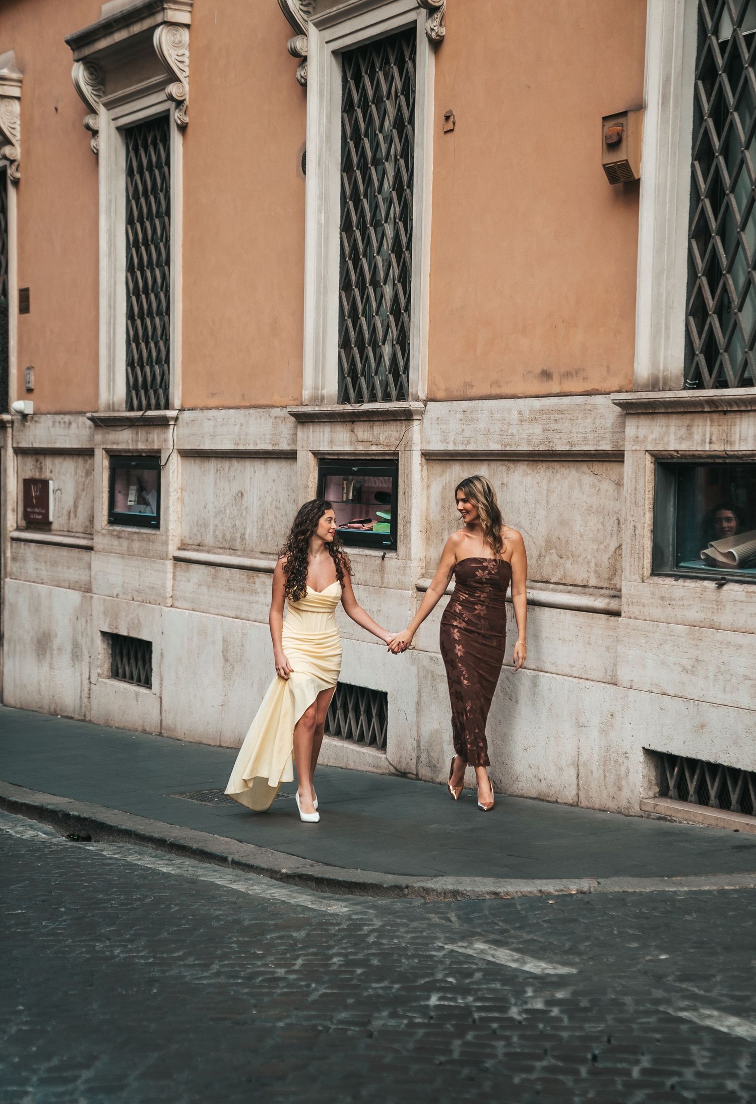 Two people walking hand in hand down a cobblestone street in Rome.