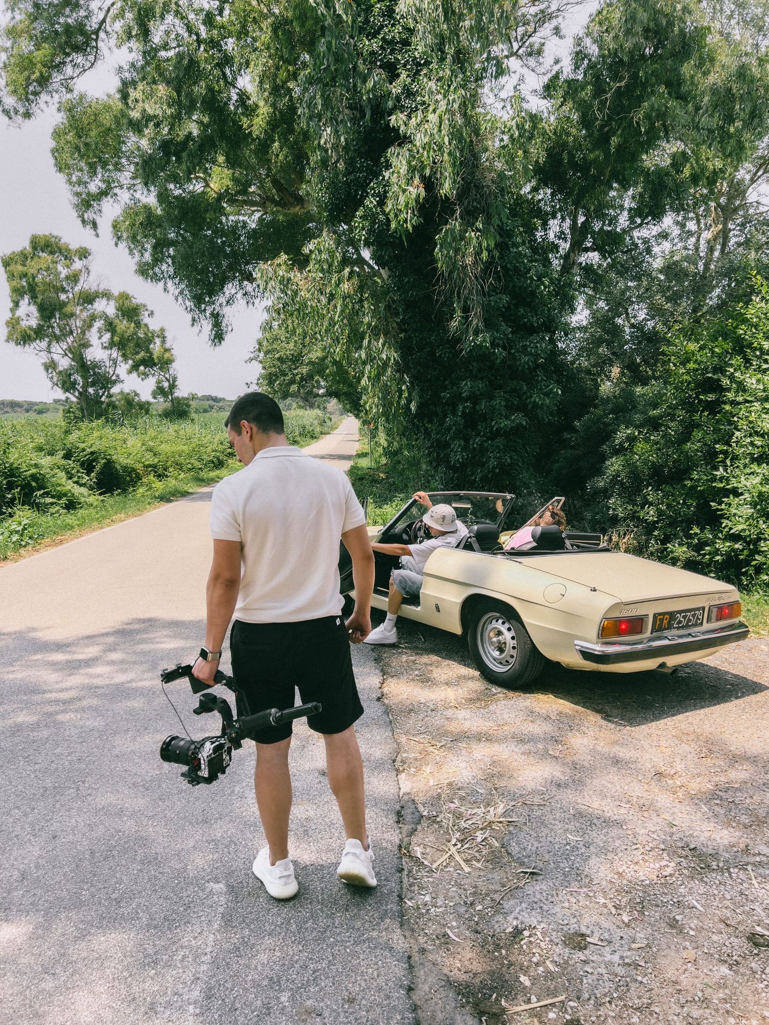 Classic vintage car parked on gravel with people walking nearby in multiple connected shots.