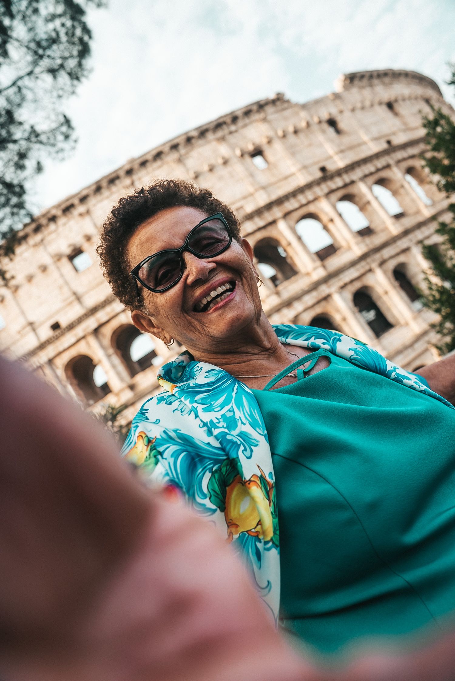 Tourist taking selfie in front of the iconic Colosseum in Rome on a bright day.