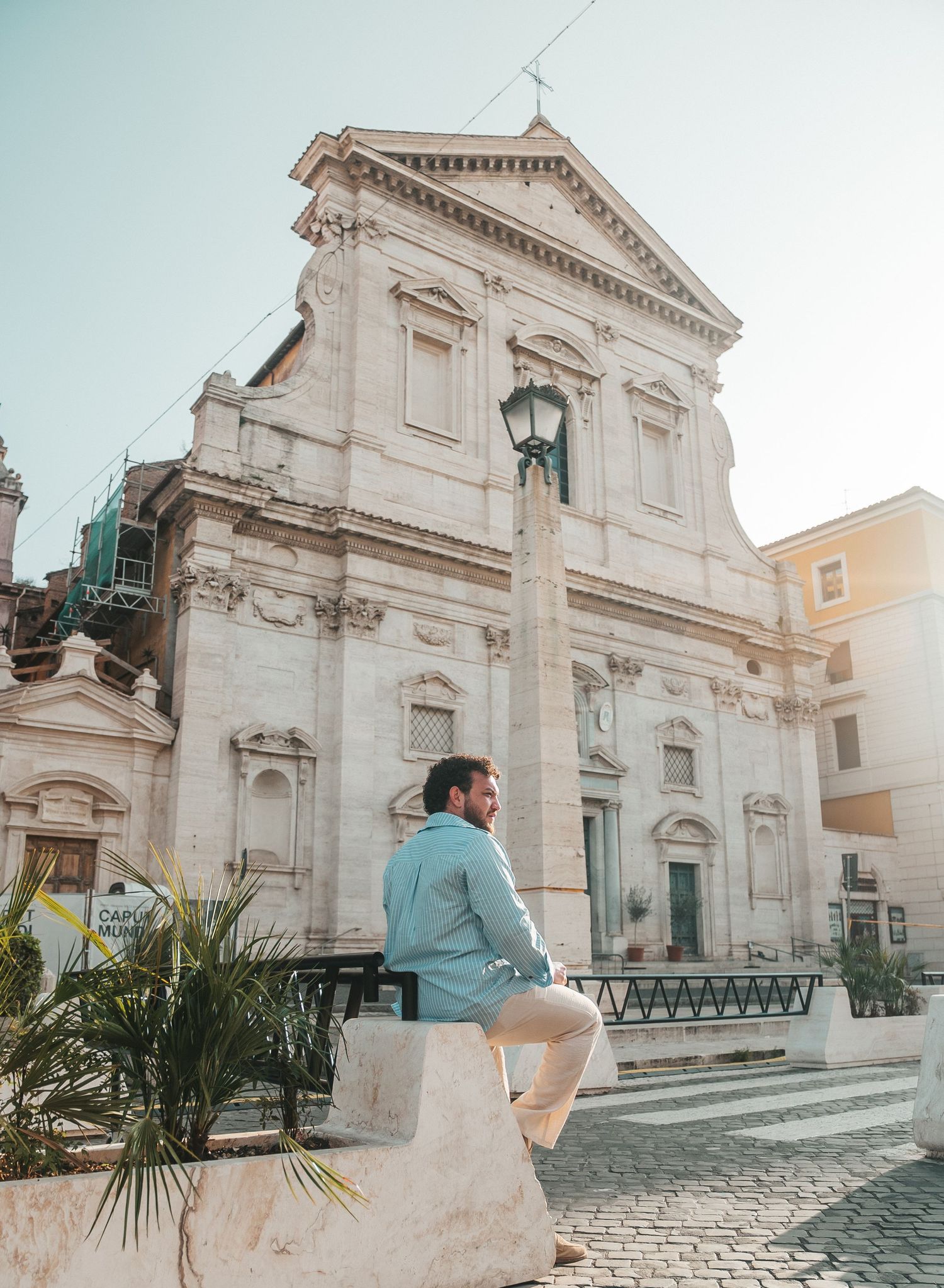 Tourist admiring the ornate white facade of a historic Italian church with classical architecture and palm trees.