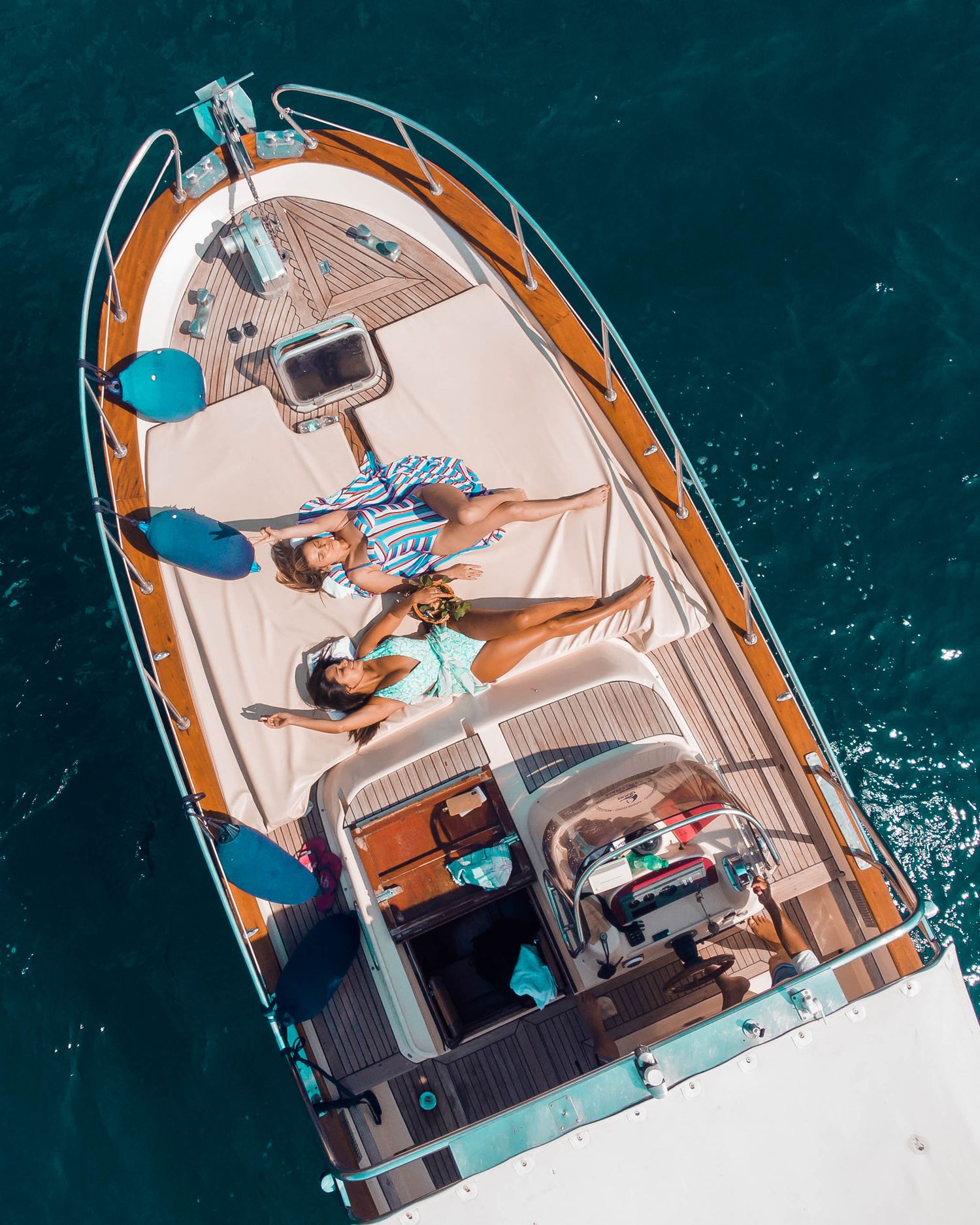Aerial view of people lounging on a luxury yacht deck with turquoise waters below.