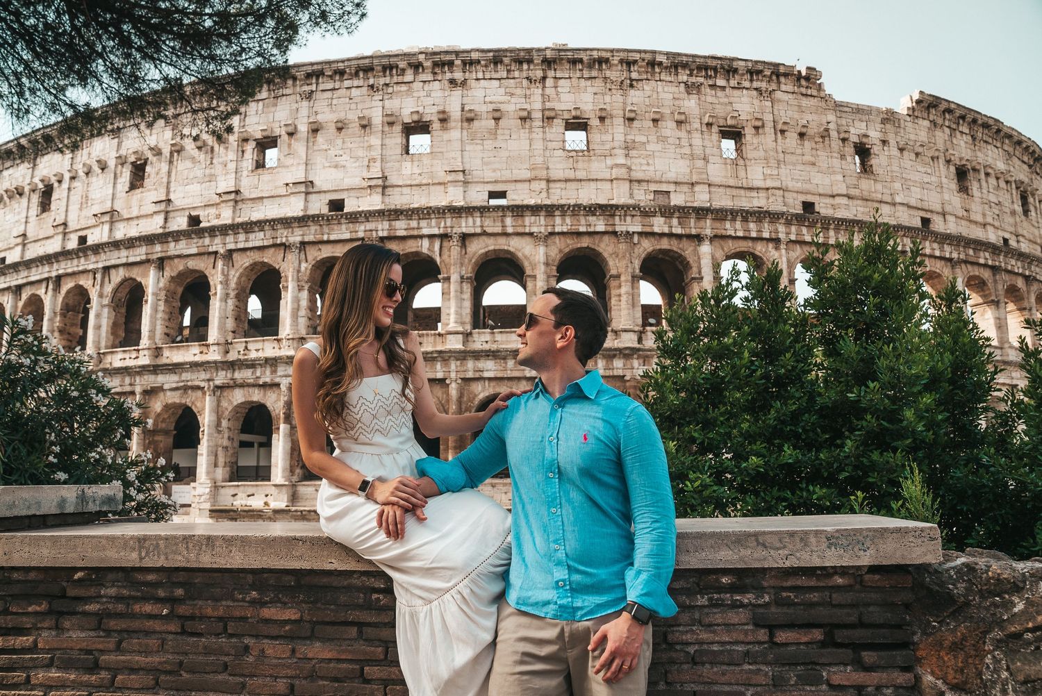 A couple poses together at different angles in front of the ancient Roman Colosseum during sunset.