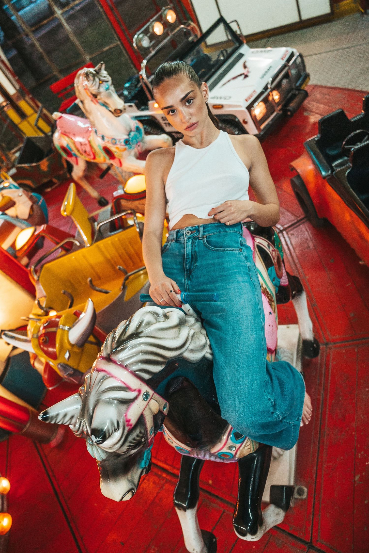 A person in a white crop top and blue jeans performs dynamic dance moves in a red-lit studio space.