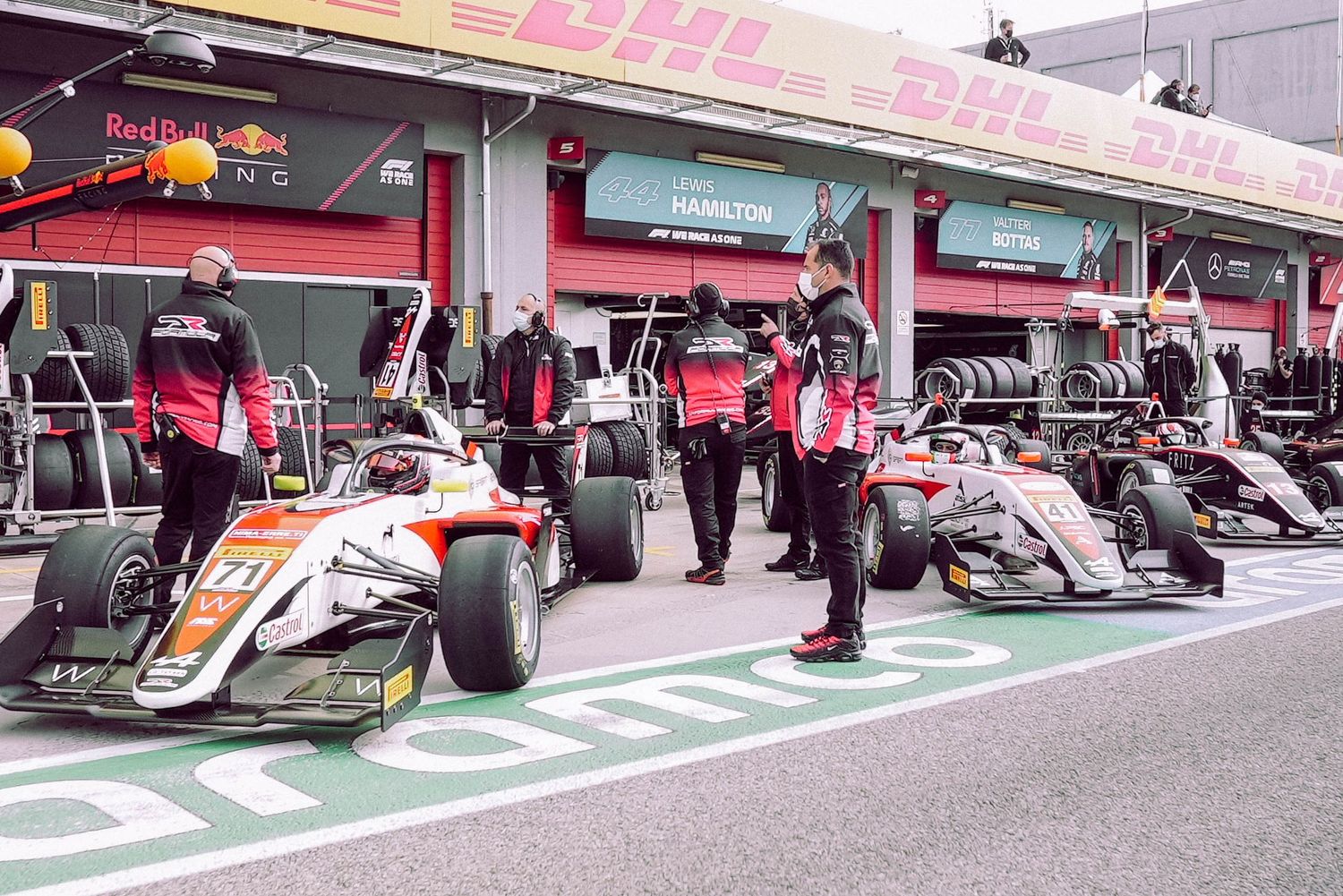 Row of Formula 1 race cars parked in pit lane with red awnings and green markings on the ground.