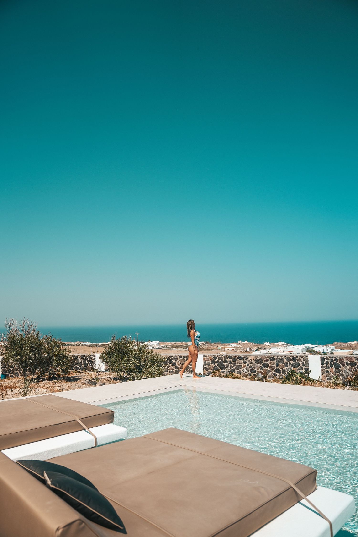 Luxurious beige sunbeds beside an infinity pool overlooking a turquoise ocean on a sunny day.