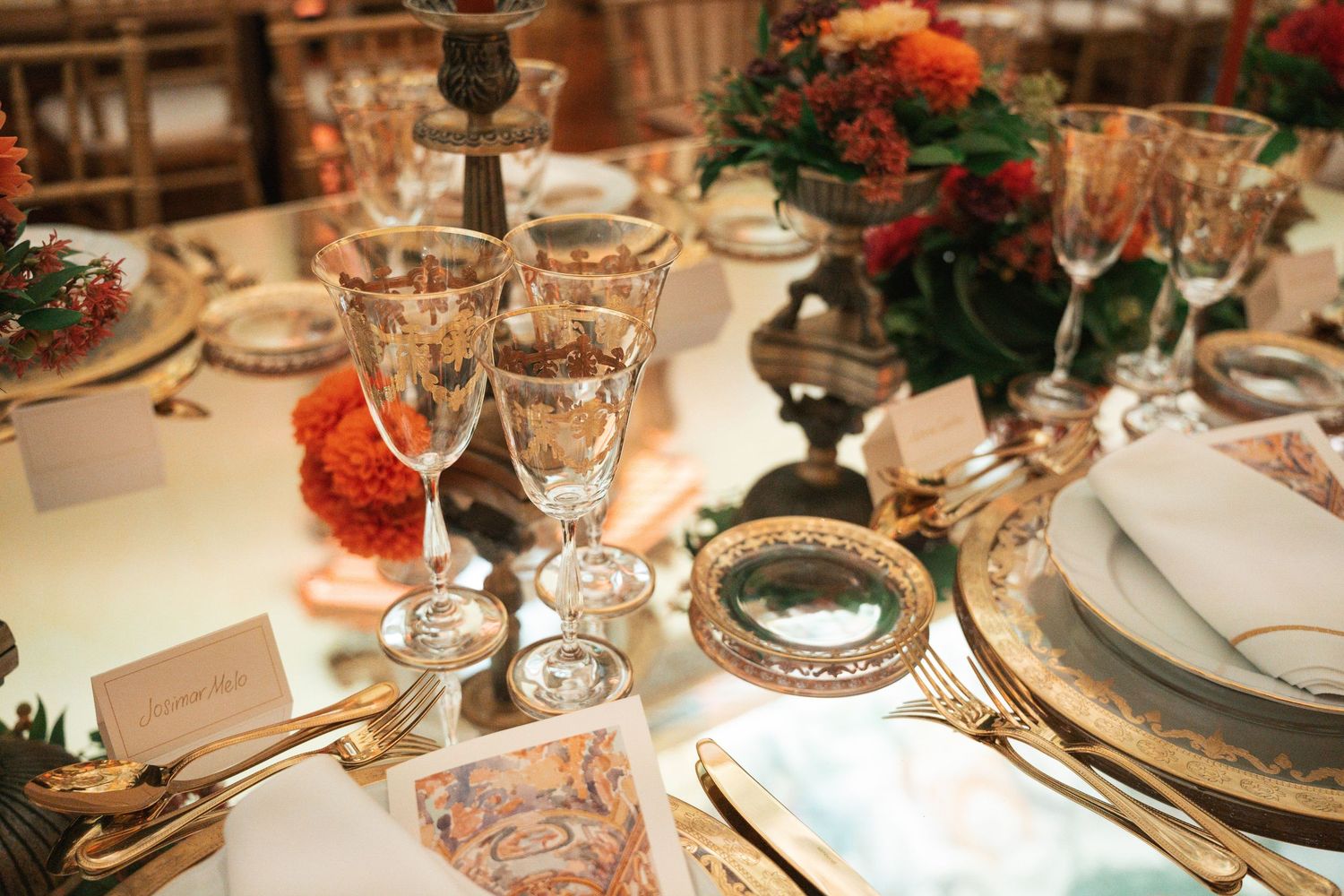Elegant wedding reception table settings with crystal glasses, white plates, and red floral centerpieces.