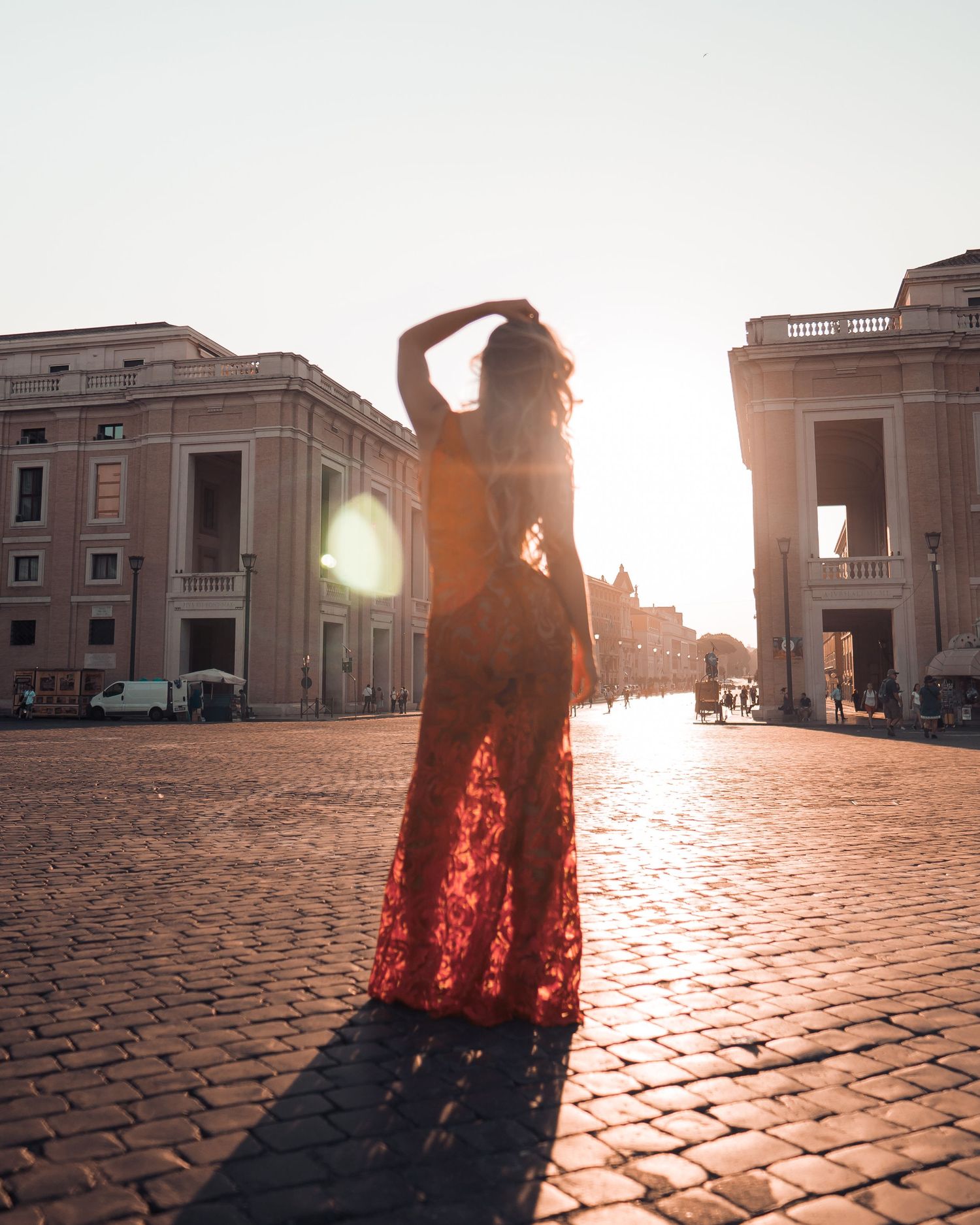 A woman in a flowing red dress dances gracefully on cobblestone streets at sunset, creating dramatic shadows.