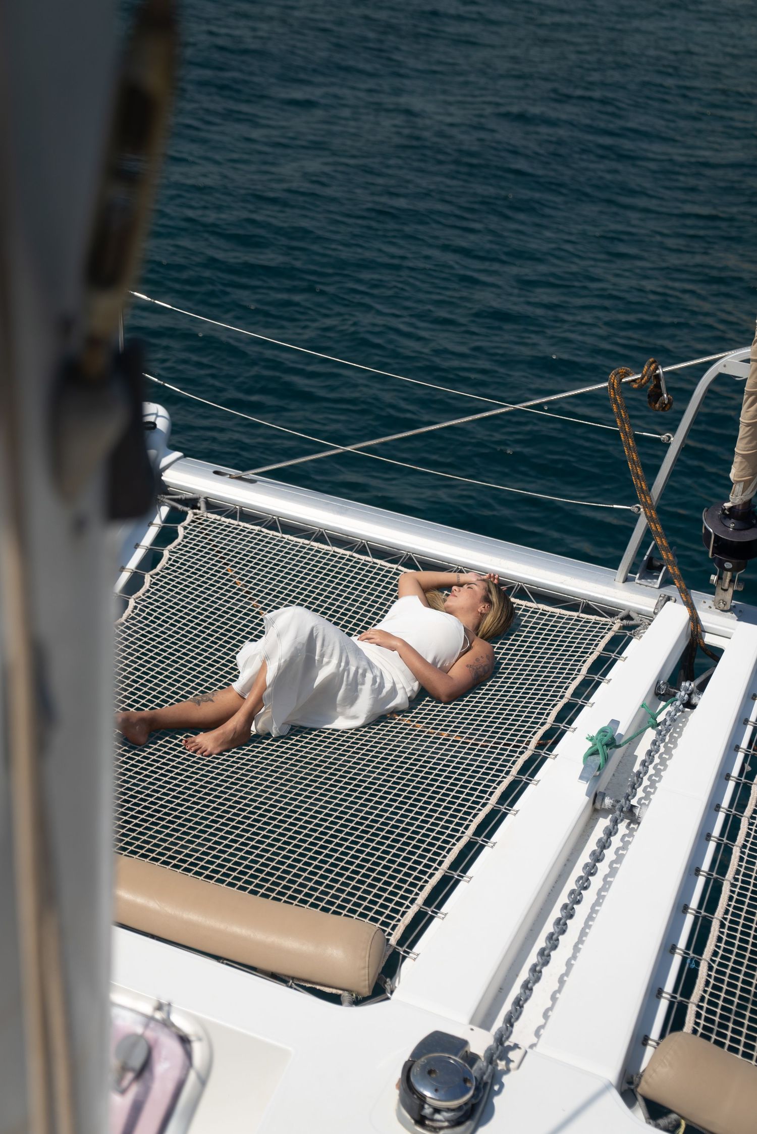 A person relaxes on the mesh netting of a catamaran sailboat while cruising on blue tropical waters.