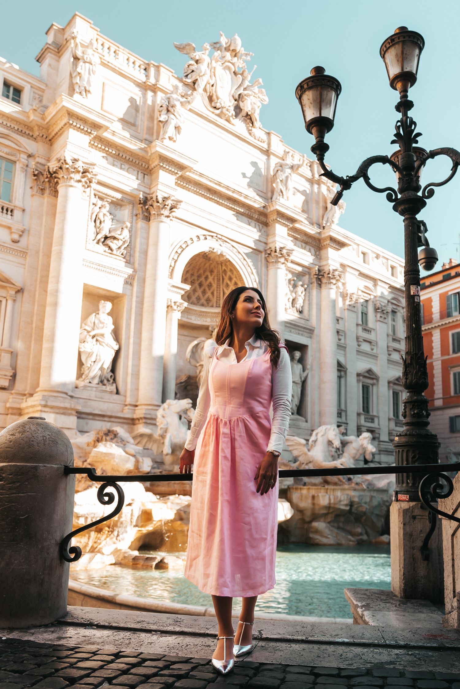Woman in pink dress posing by the ornate Trevi Fountain in Rome.