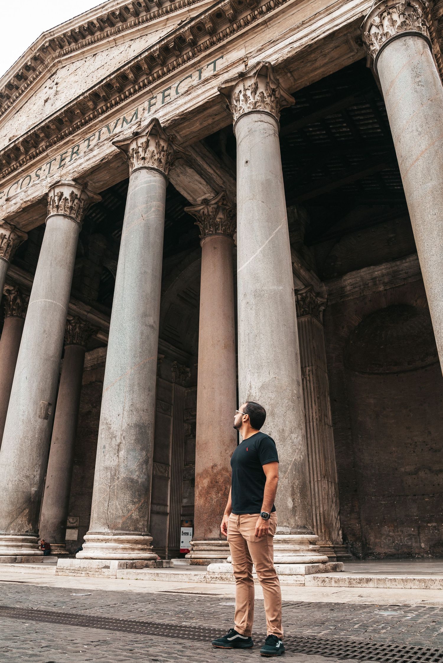 A person walks past ancient Roman columns at the Pantheon in Rome, creating a dramatic architectural perspective.