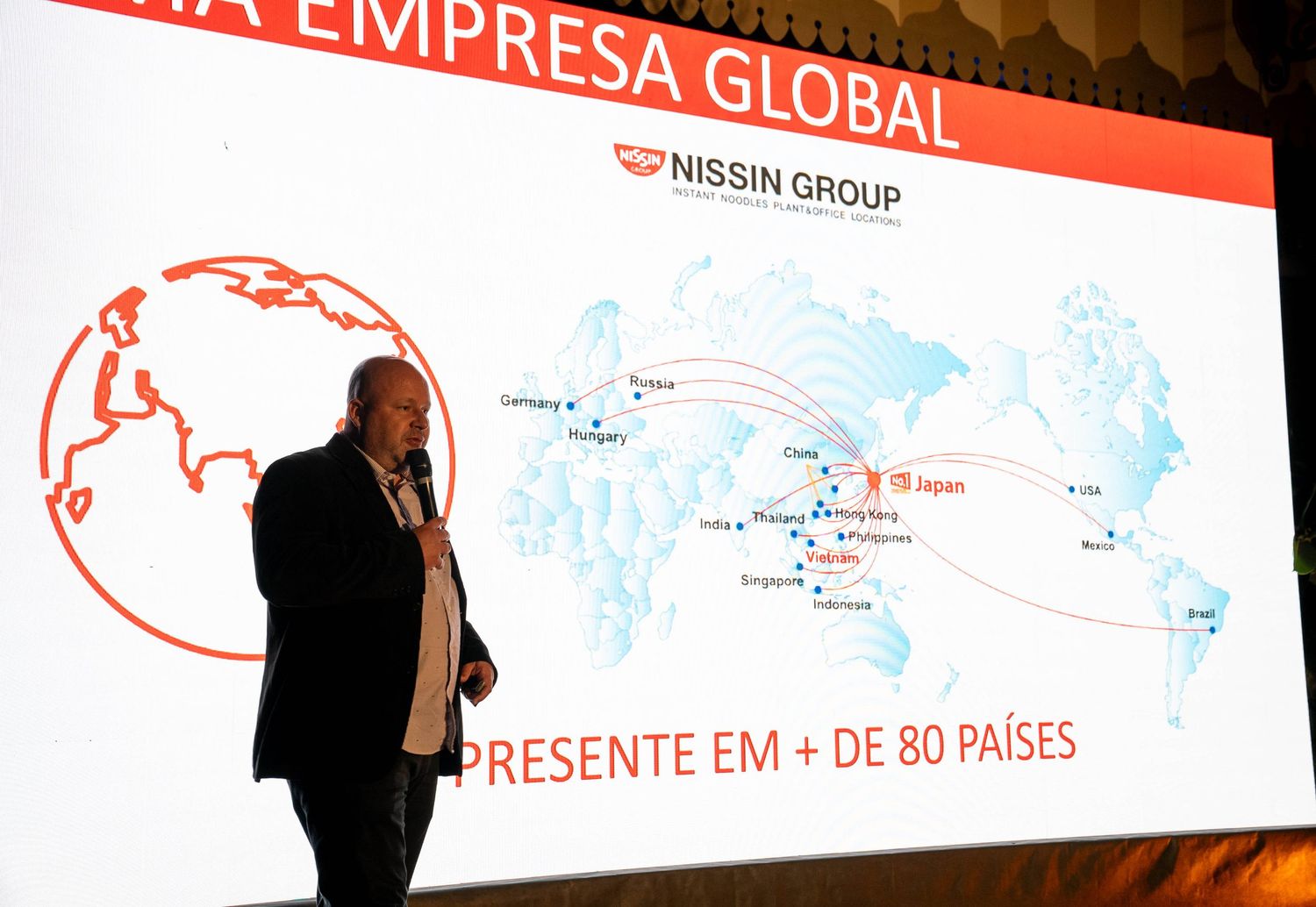 Business presentation slide showing Nissin Group global presence map with silhouette of speaker against projection screen.