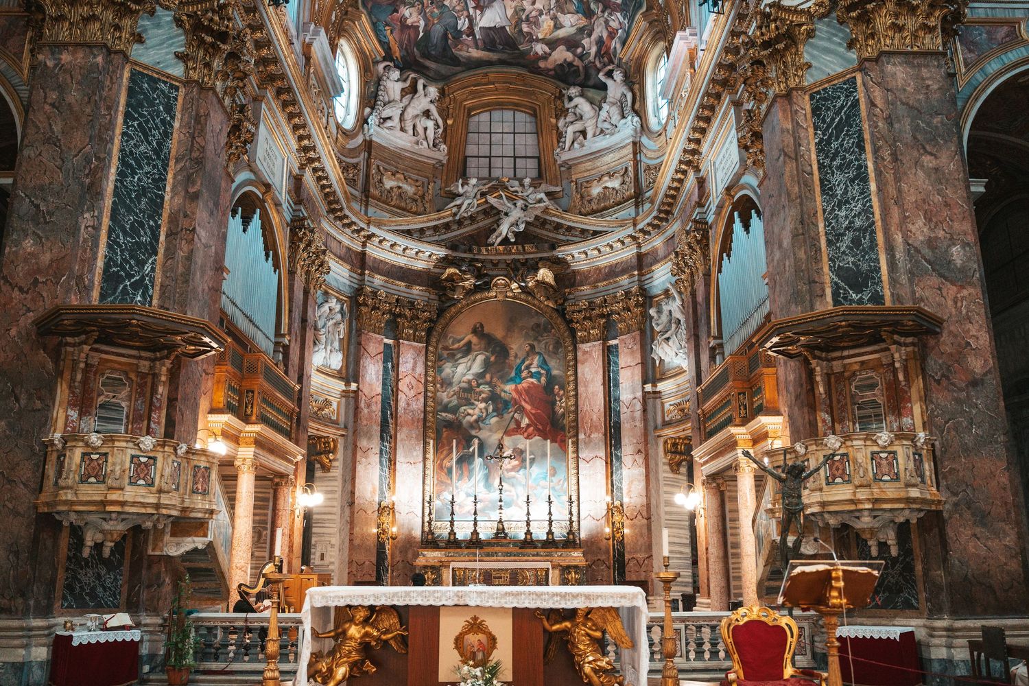 Ornate baroque church interior with gilded decorations, frescoed ceiling, and marble altar illuminated by warm lighting.