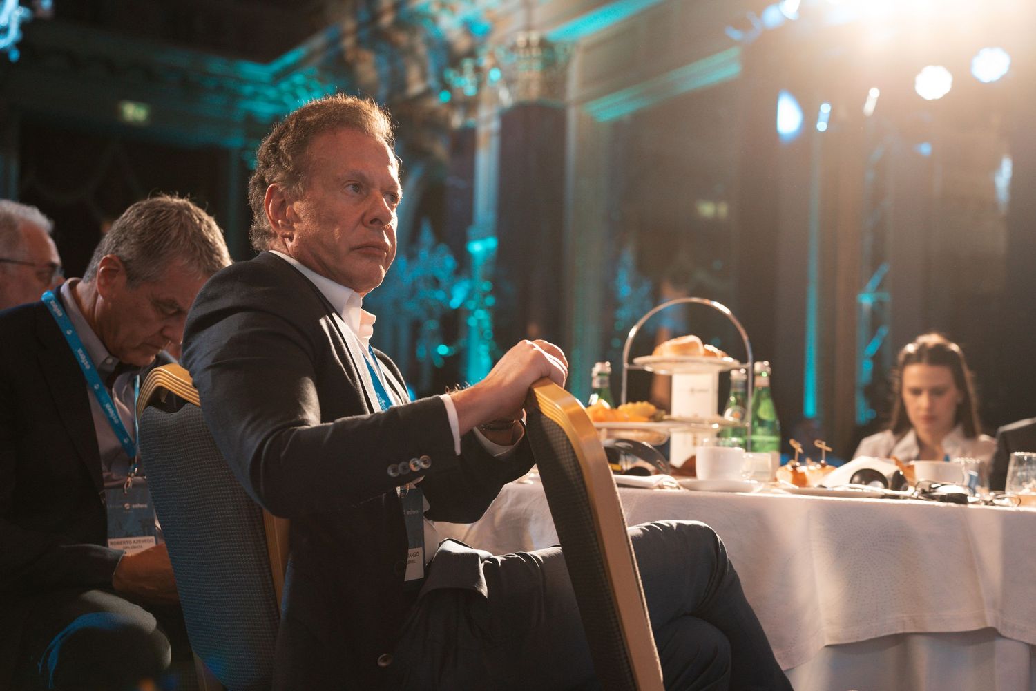 A group of people seated at elegant dining tables in a room illuminated with blue ambient lighting.