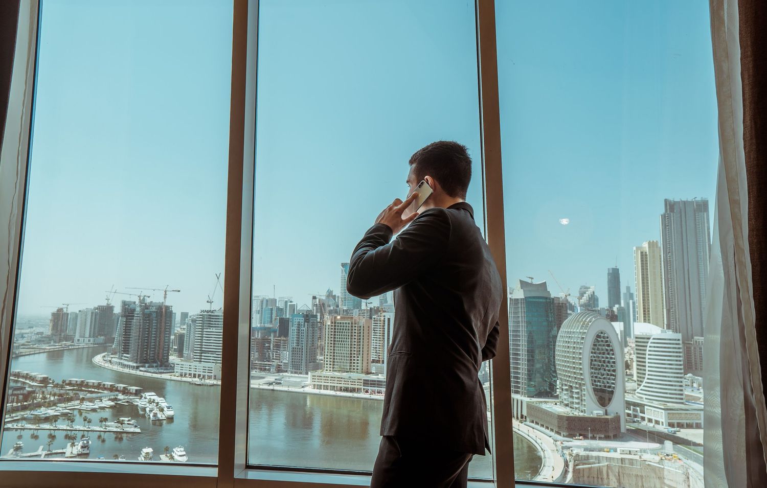 Panoramic view of a city skyline through large windows with silhouetted figures standing in front.